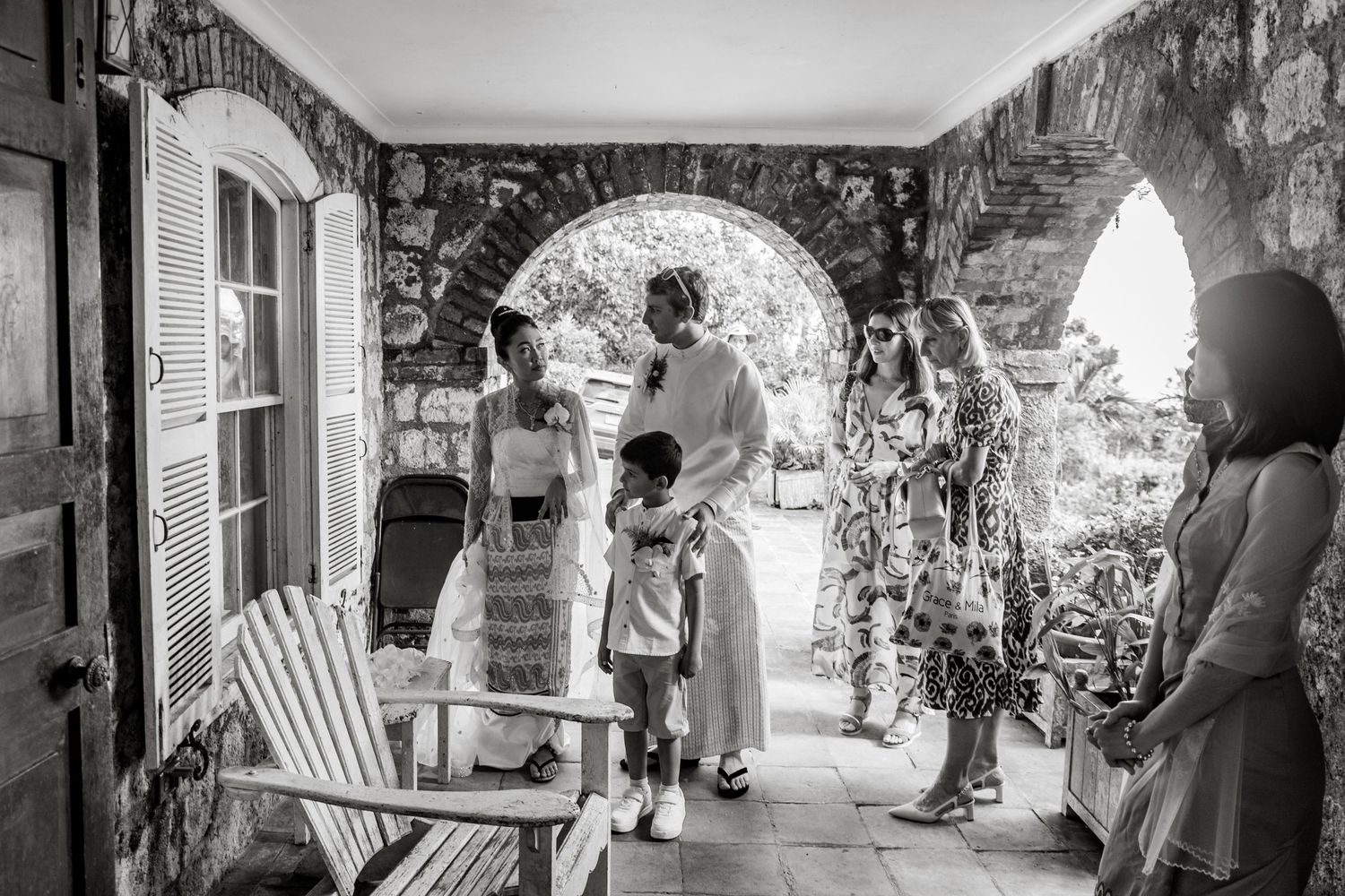 Black and white photo of a family gathering under a stone archway on a porch, sharing a warm moment together.