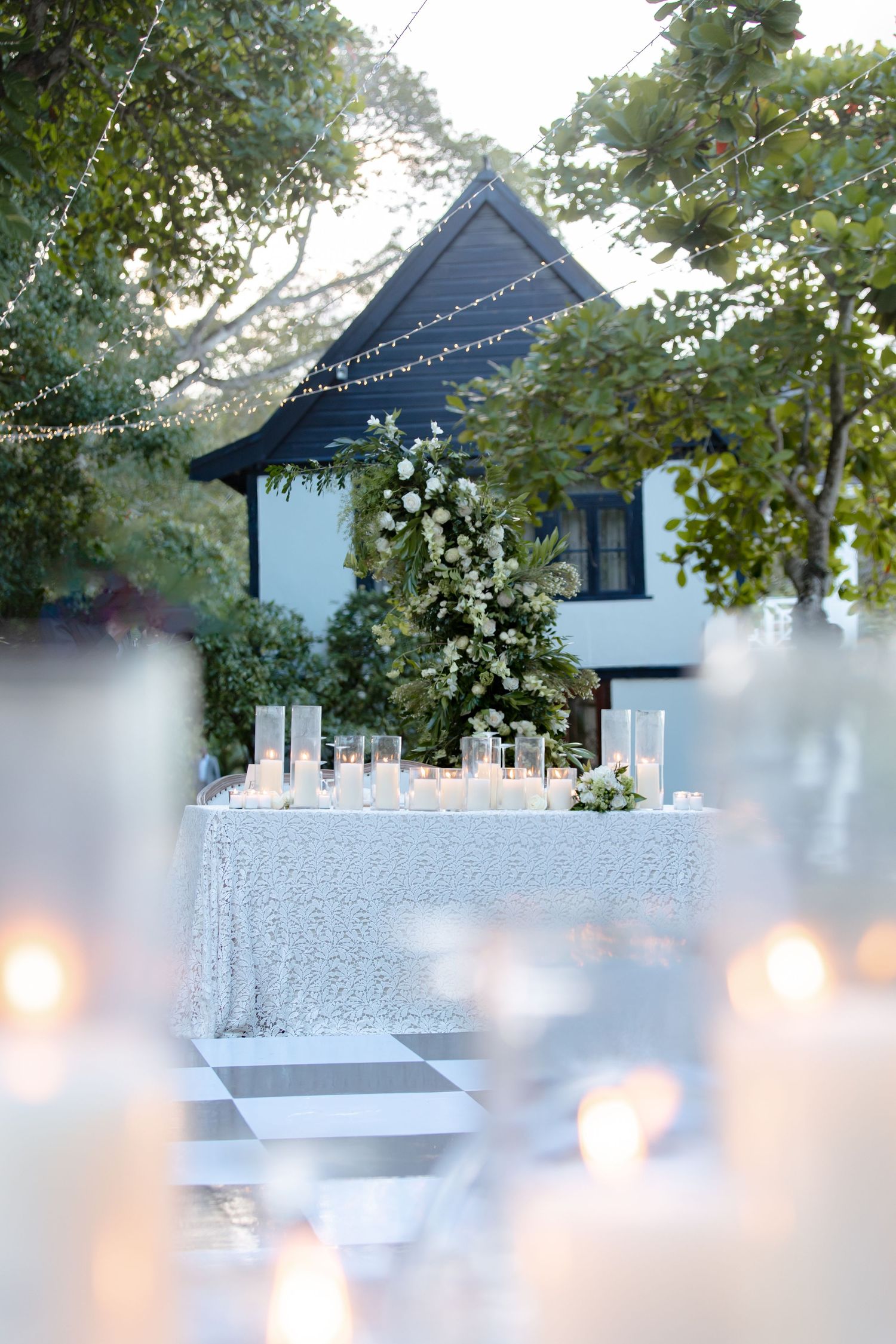 Romantic outdoor wedding reception with glowing candles, sequined sweetheart table, and floral arch at dusk.