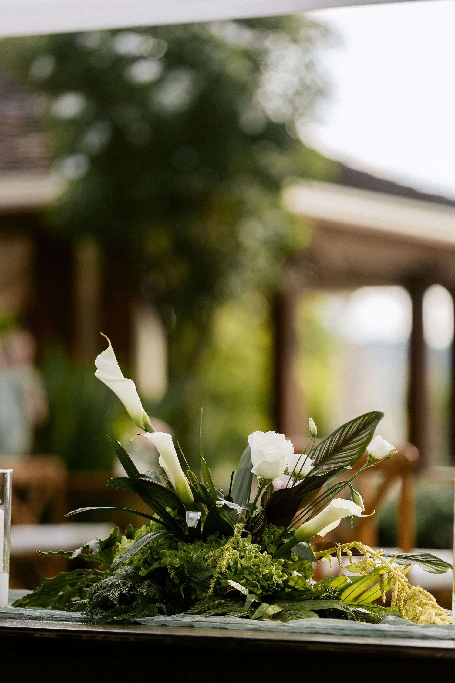 Elegant floral centerpiece with white calla lilies and lush green foliage on a table at an outdoor venue.