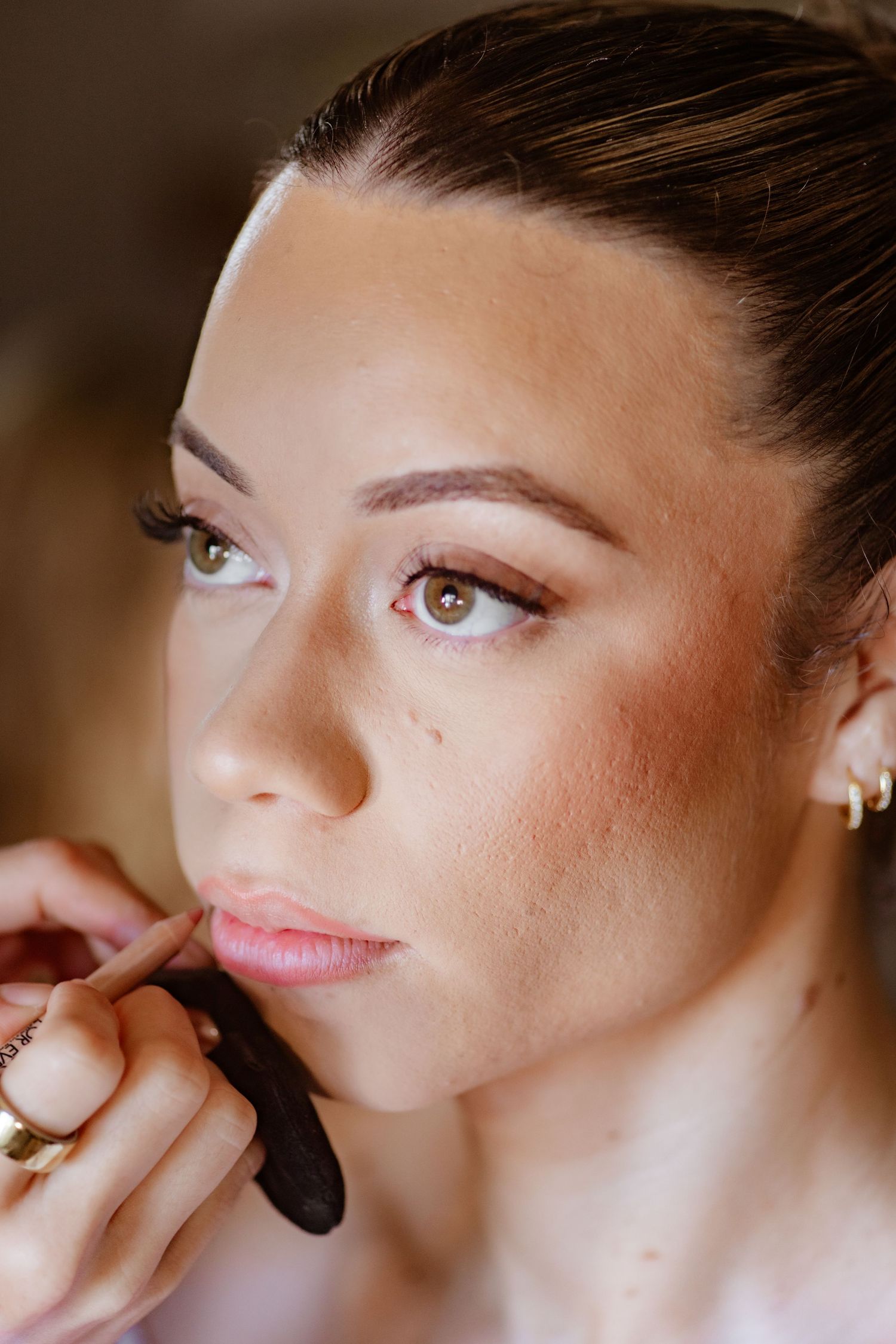 Close-up of bride getting lip makeup applied by makeup artist before wedding ceremony.