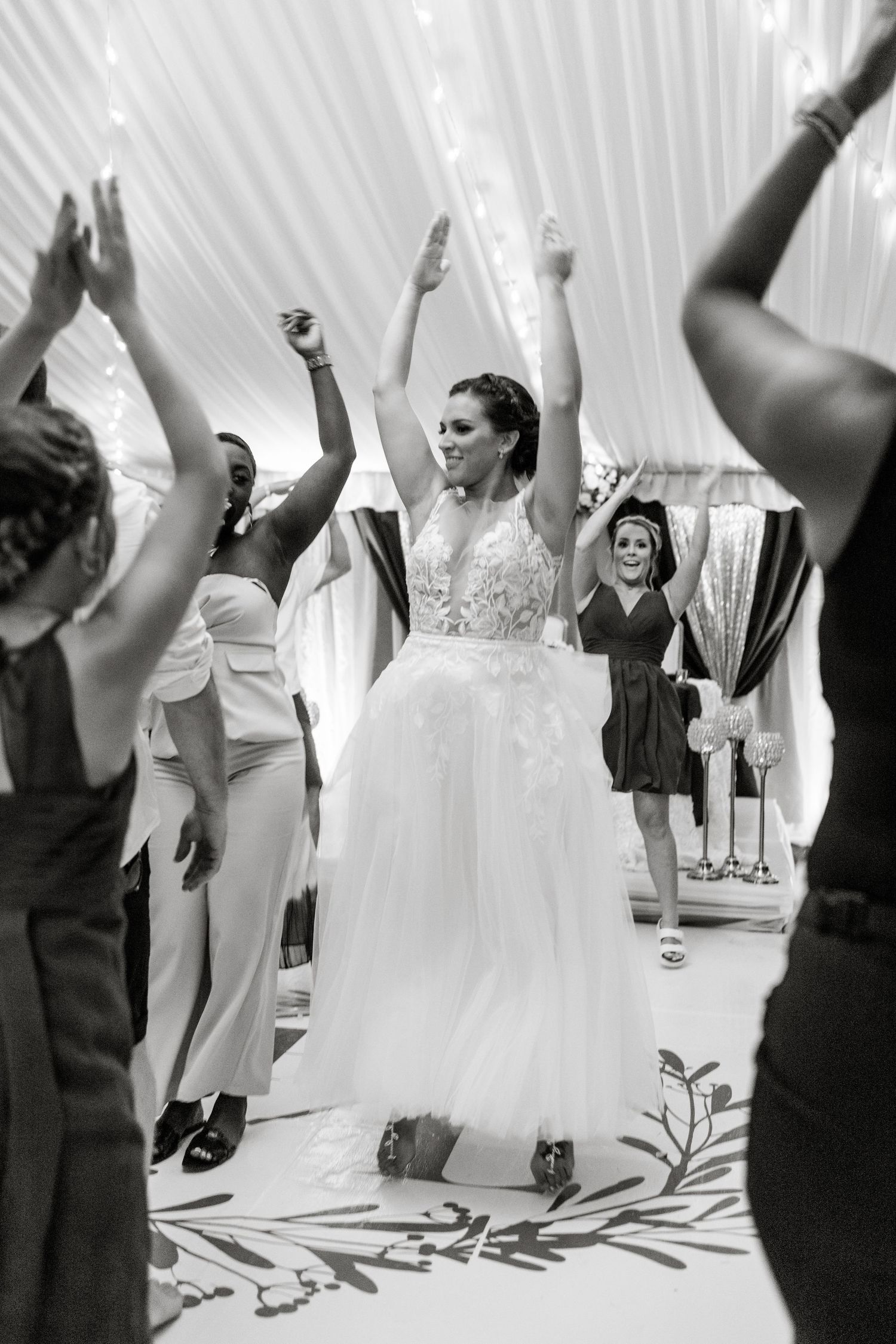 Black and white photo of bride dancing with arms raised at her wedding reception.