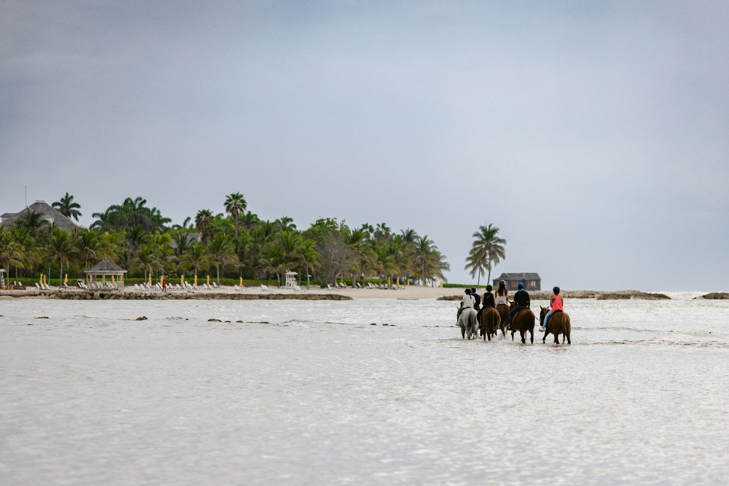 Group of horseback riders on a pristine white sandy beach with lush palm trees in the background.