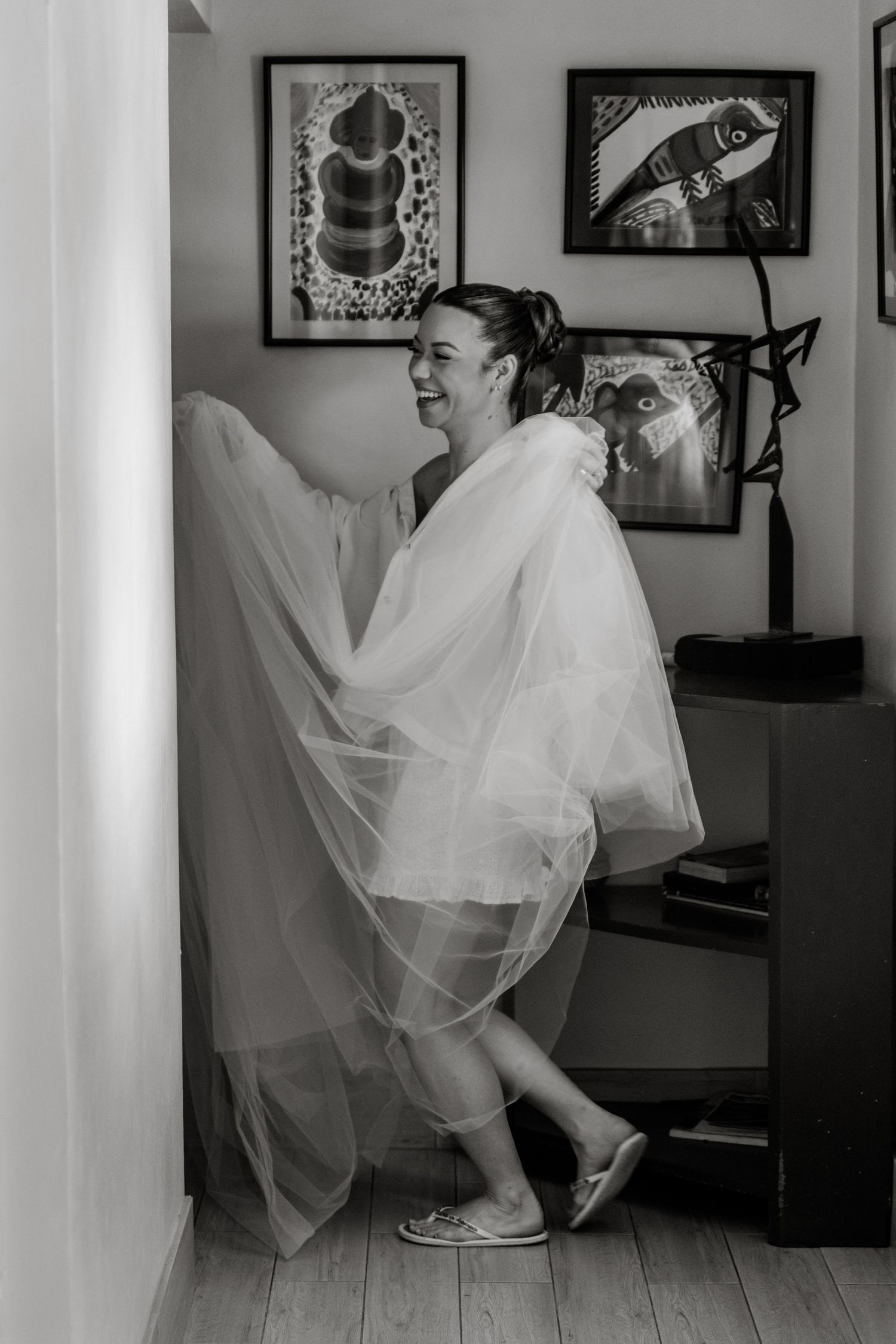 Joyful bride laughing while wrapped in flowing wedding veil in black and white photo.