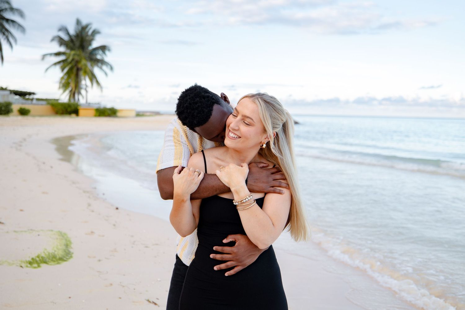 Happy interracial couple hugging on a sunny tropical beach with palm trees.