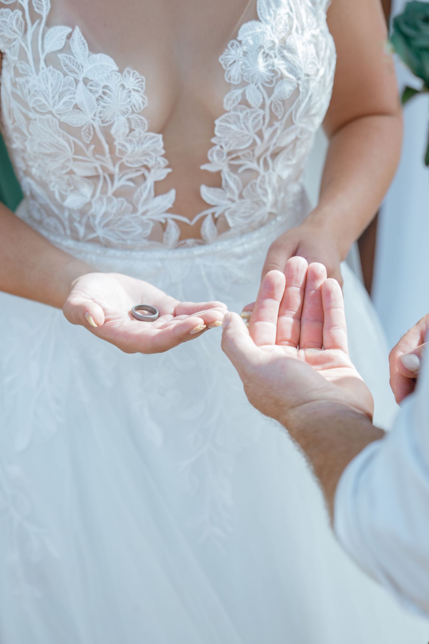 Bride in lace wedding dress holds wedding rings in her palm during outdoor ceremony.