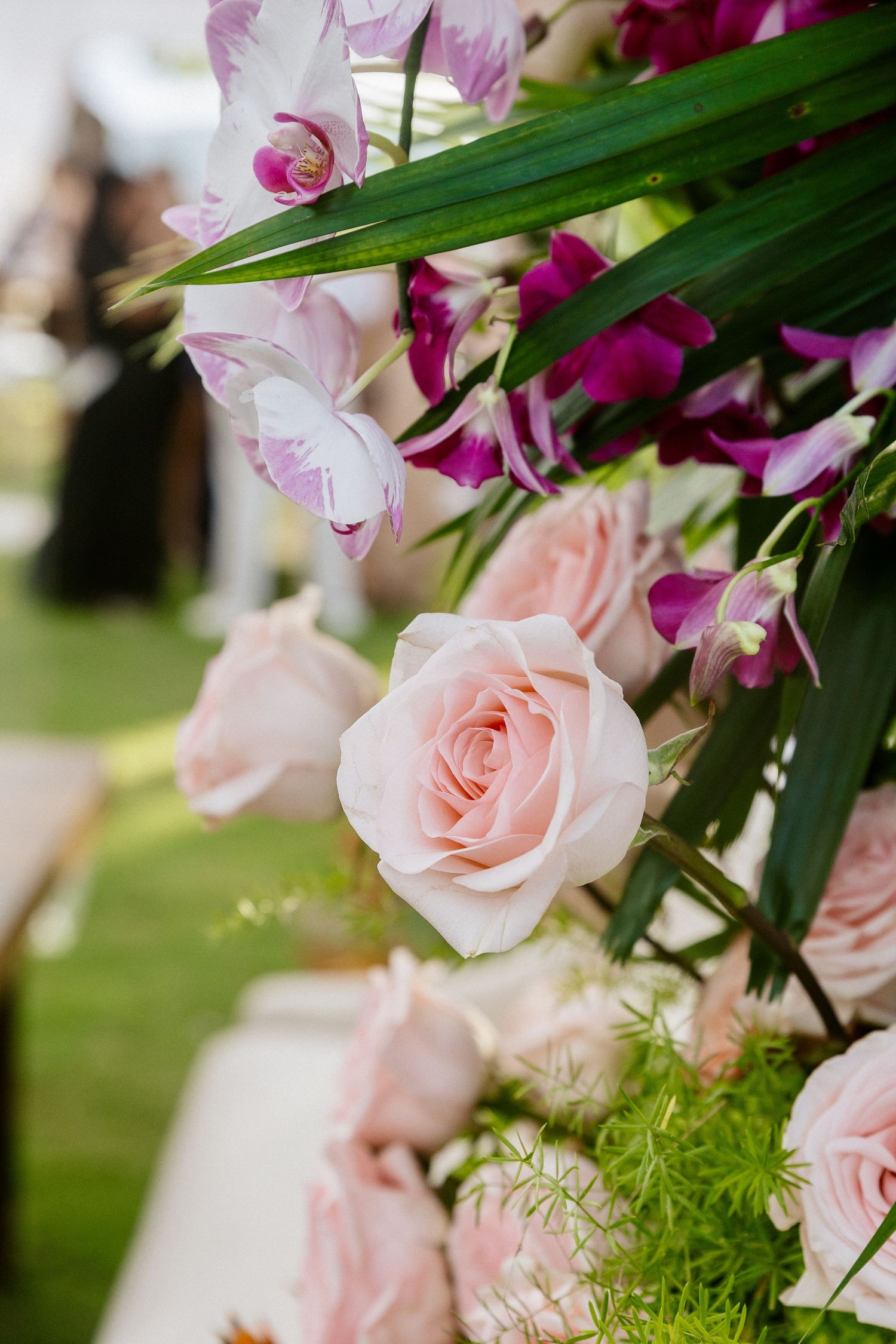 Close-up of elegant pink roses and purple orchids with green tropical leaves in a wedding floral arrangement.