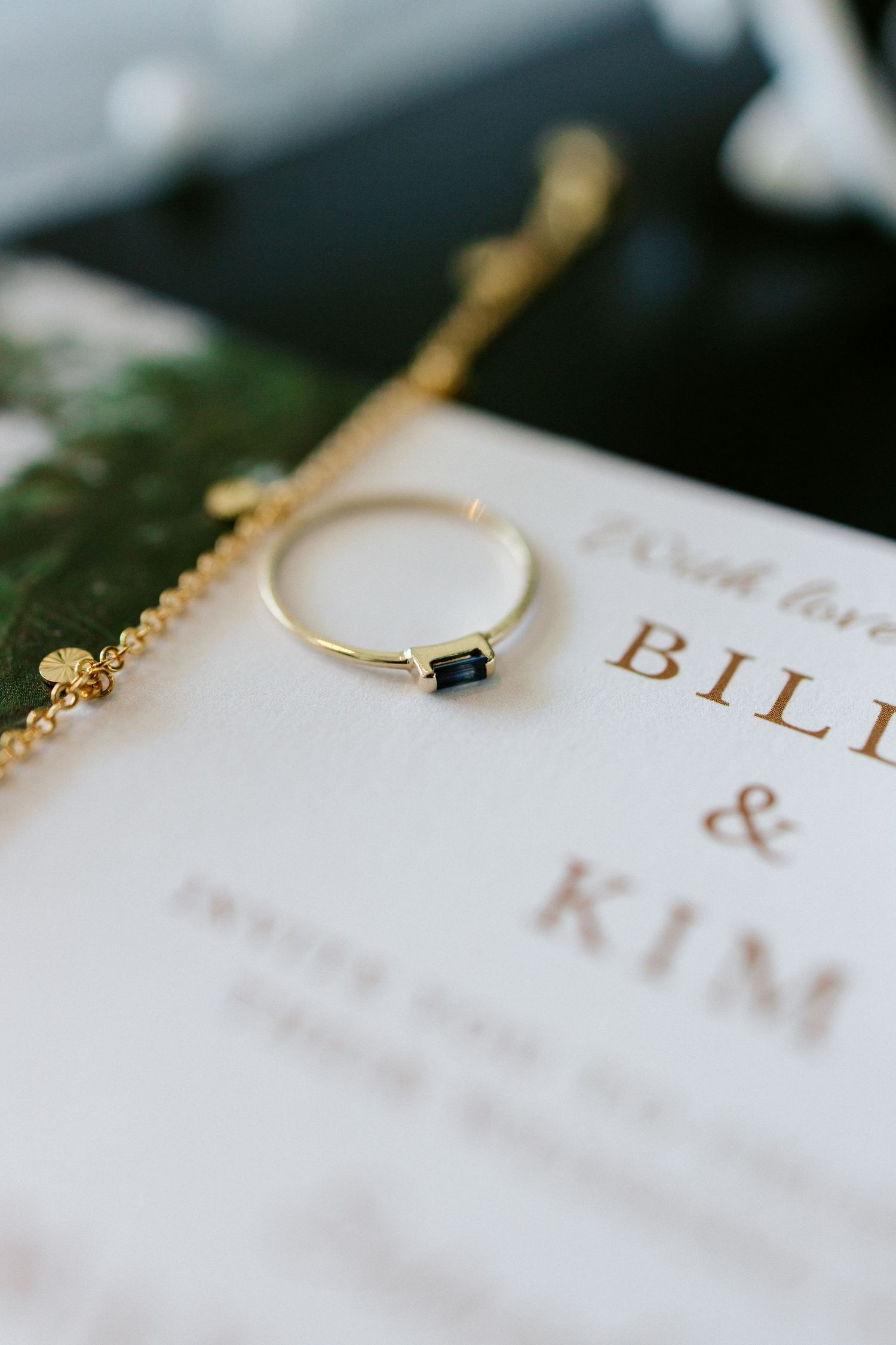 Gold ring with sapphire baguette stone resting on wedding invitation for Bill and Kim.