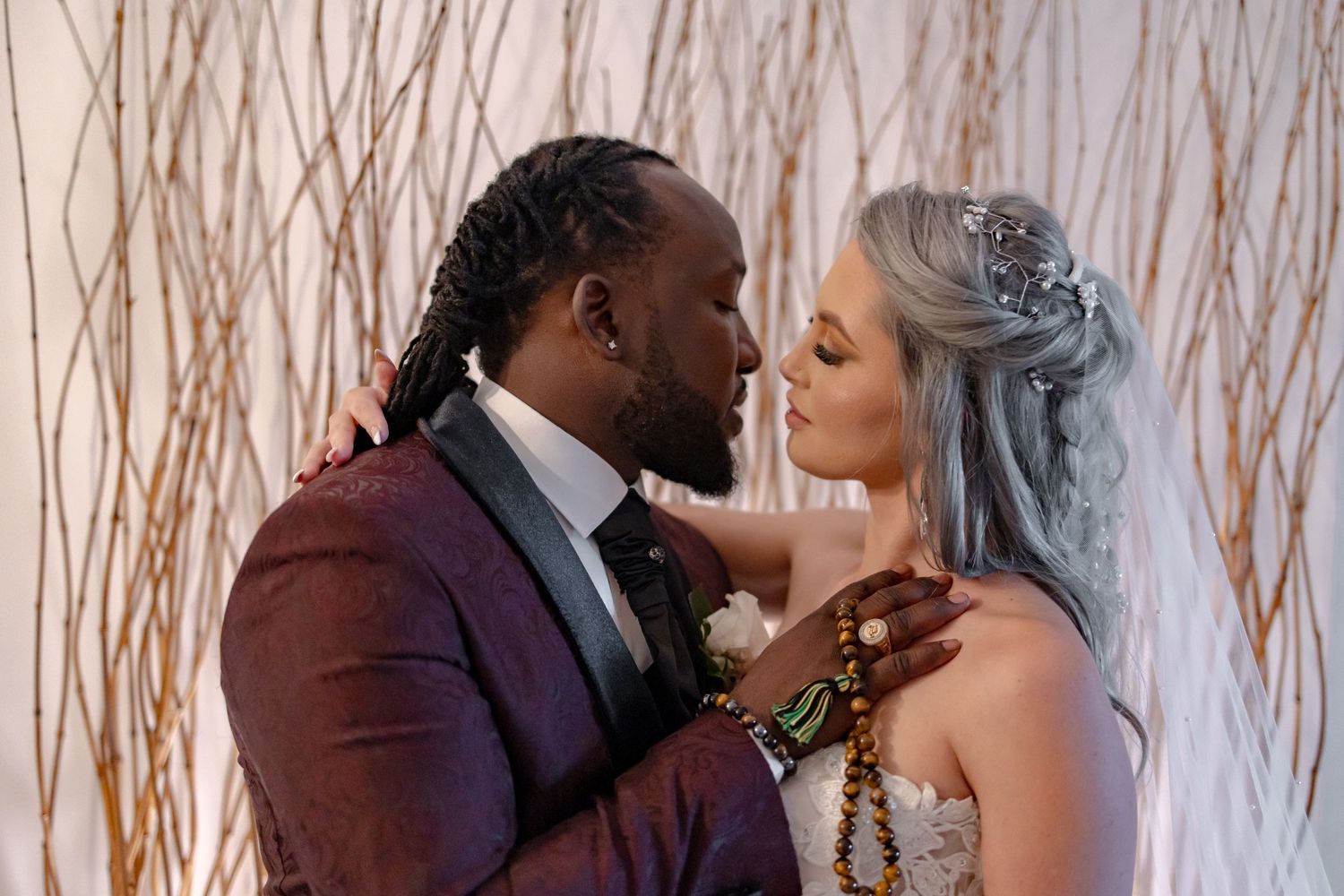 Interracial wedding couple shares an intimate moment in front of a golden branch backdrop.
