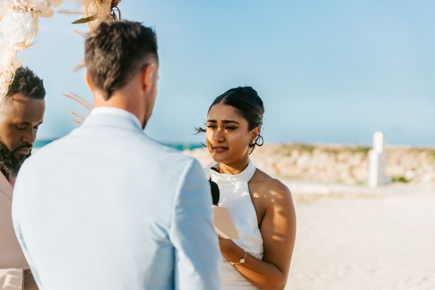 Bride and groom exchanging vows at a romantic beach wedding ceremony under a clear blue sky.