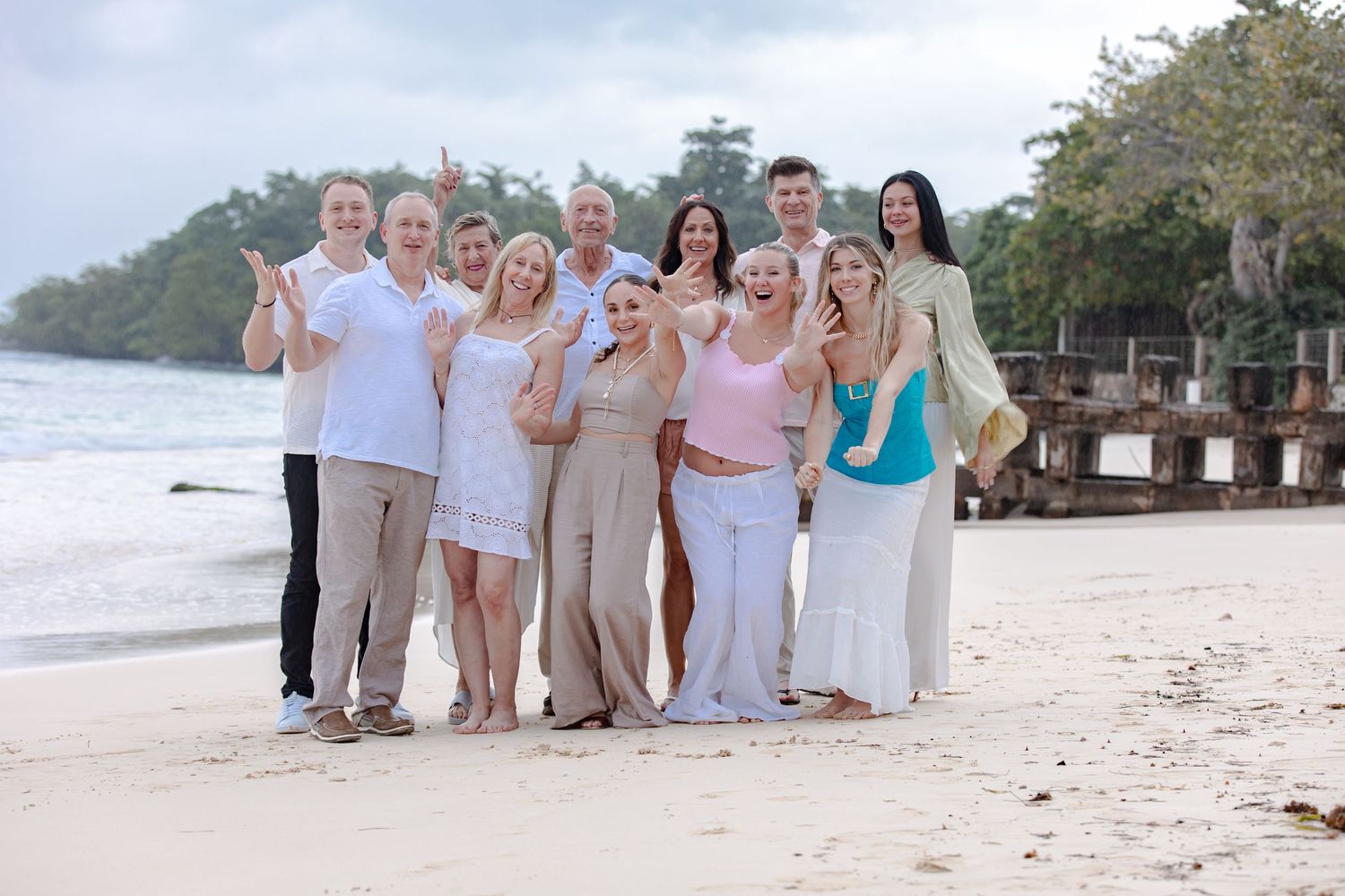 Large group of smiling people posing together on a tropical sandy beach vacation.