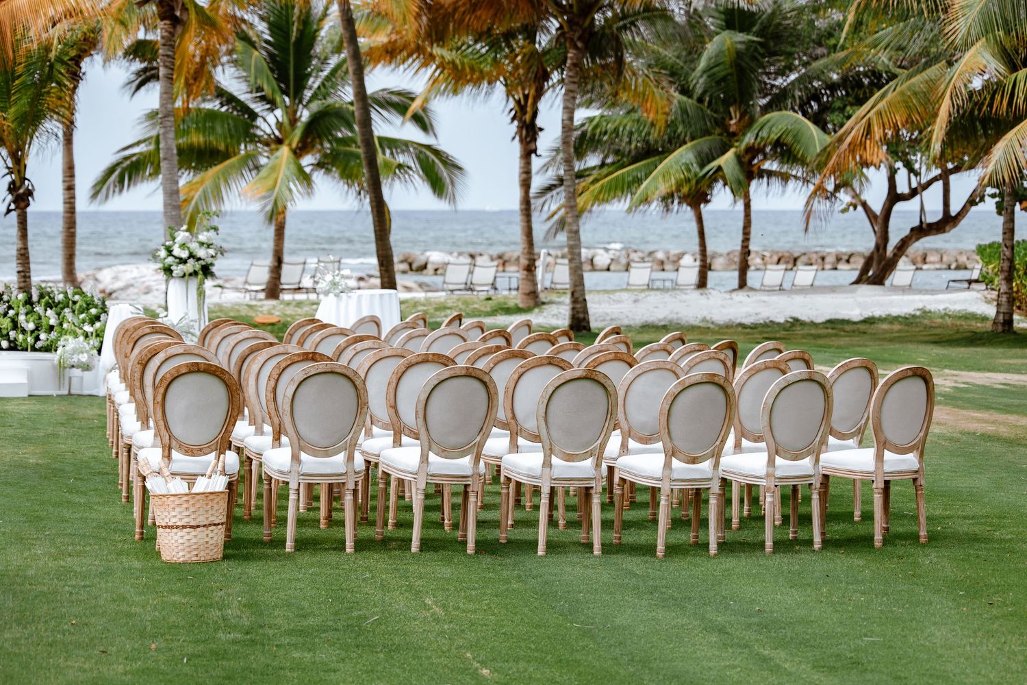 Rows of ornate gold and white chairs arranged on green grass for an outdoor wedding ceremony with ocean views.