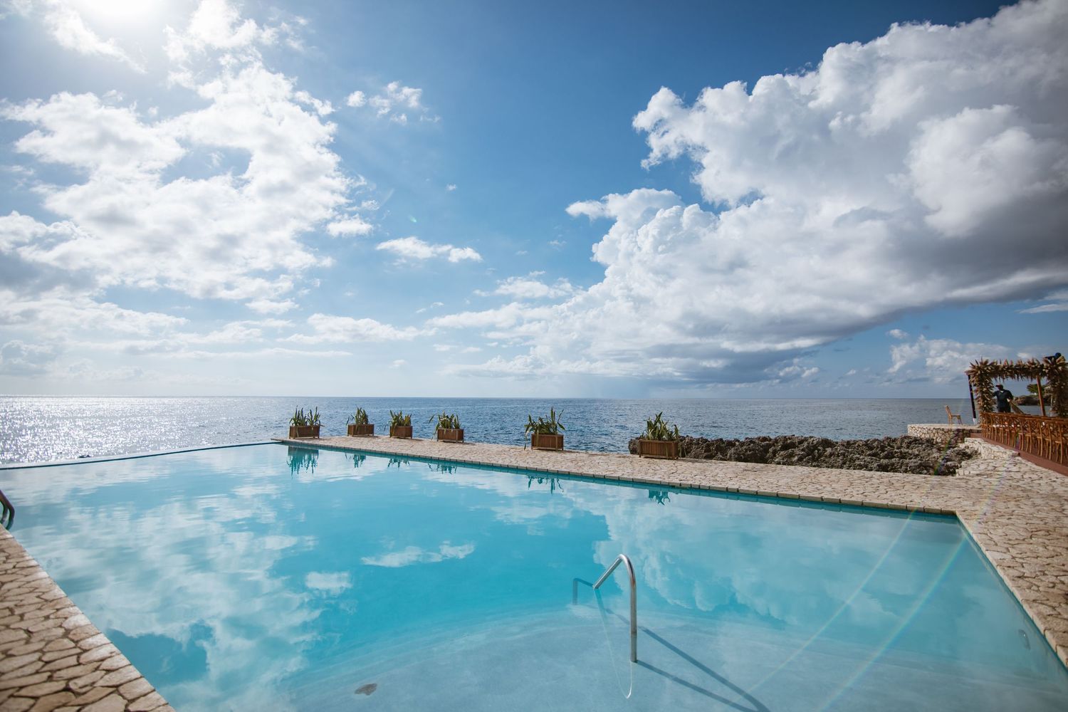 Stunning infinity pool overlooking turquoise ocean under blue sky with white clouds at luxury resort.