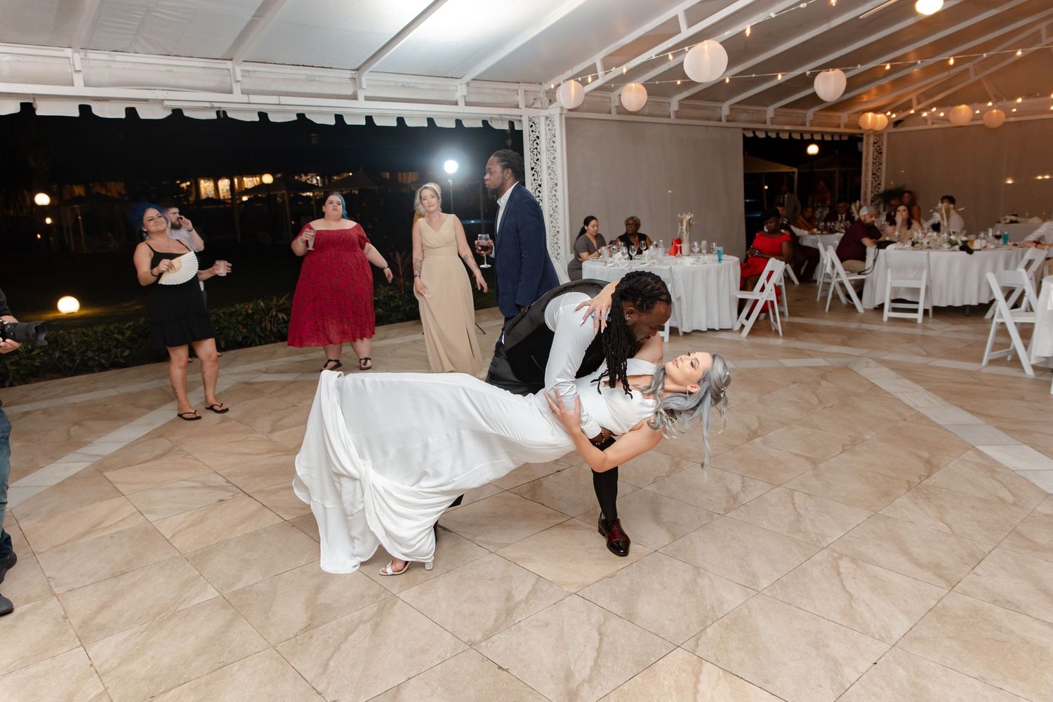Groom dramatically dips bride in white wedding gown on dance floor at outdoor tented reception.