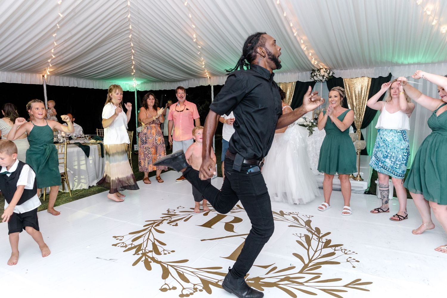 Man jumping energetically on the dance floor at a wedding reception surrounded by guests.
