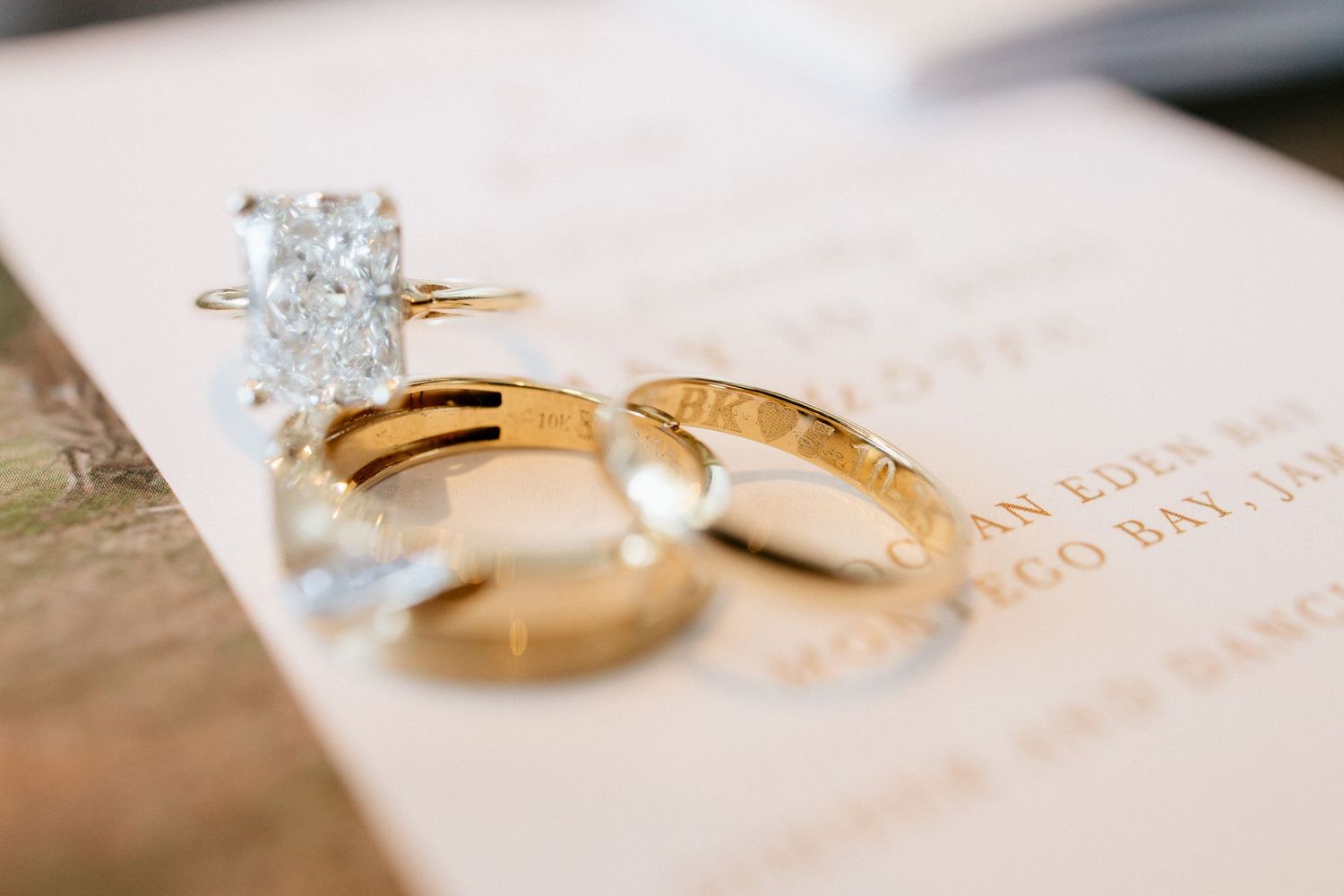 Gold wedding bands and diamond engagement ring resting on elegant wedding invitation stationery.