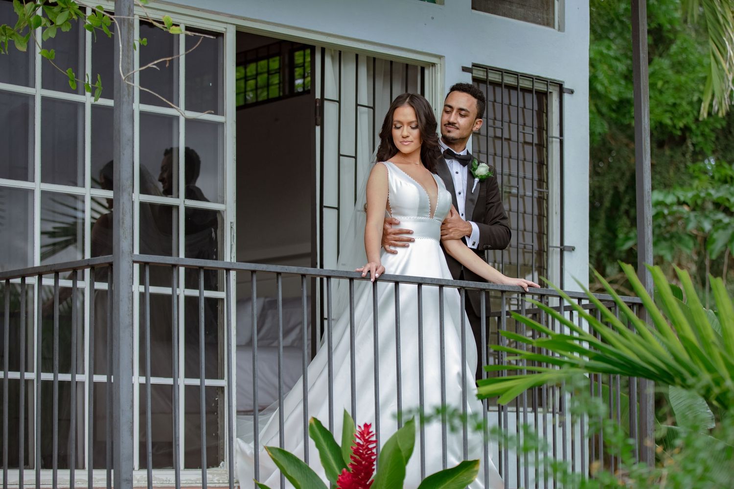 Elegant bride and groom stand together on a balcony with tropical greenery at wedding.