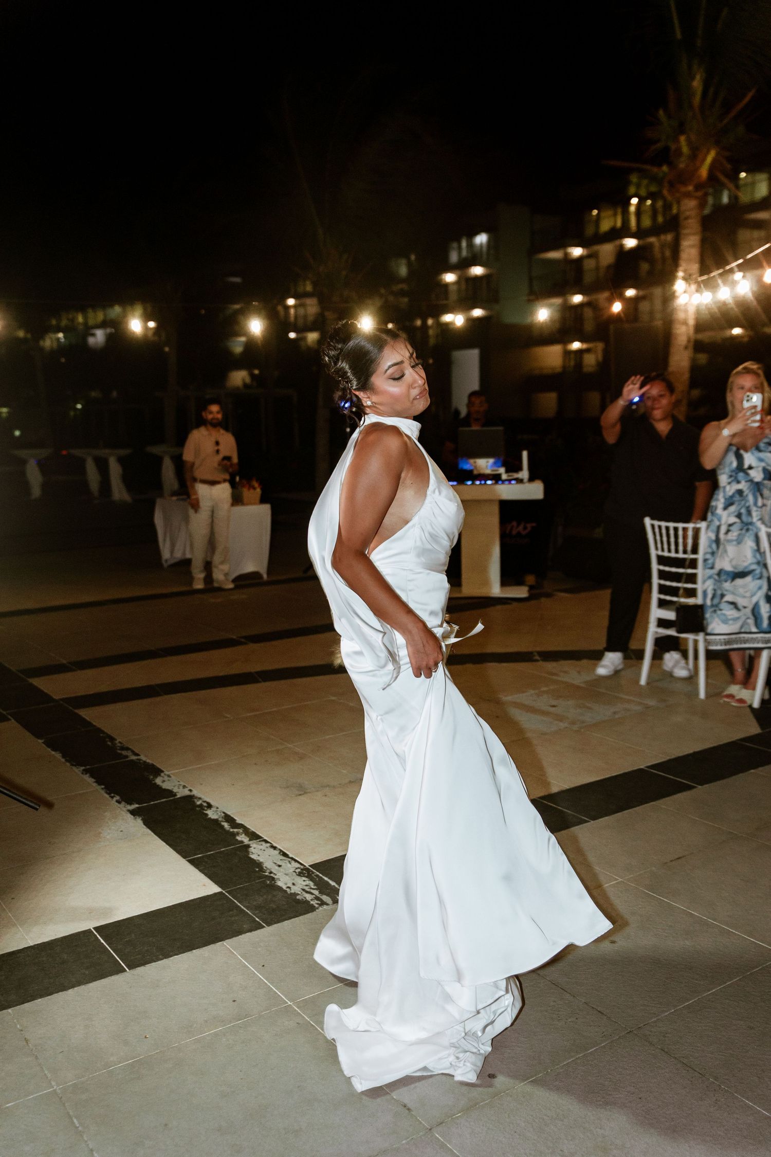 Bride in a white satin halter gown dances at outdoor nighttime wedding reception.