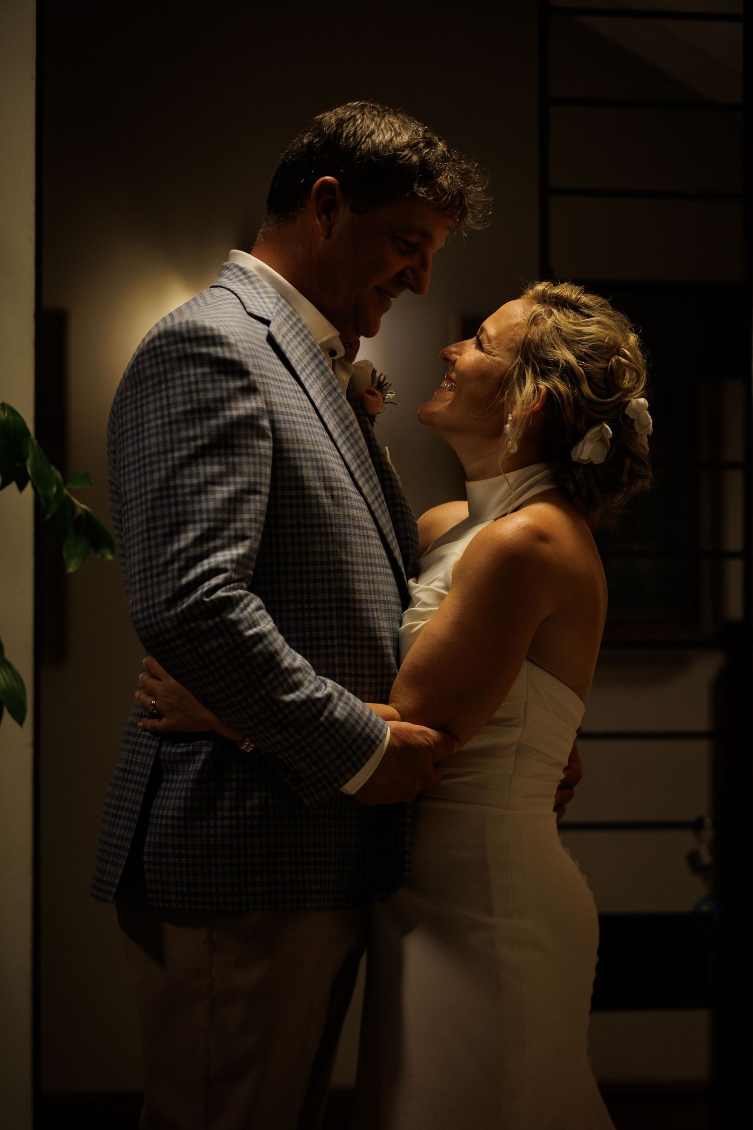 Bride and groom share romantic embrace in warm dim indoor lighting during evening wedding celebration.