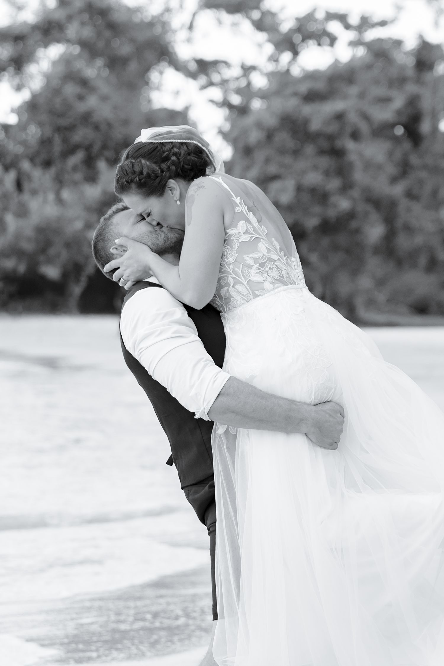Black and white photo of groom lifting bride for a romantic kiss on the beach.