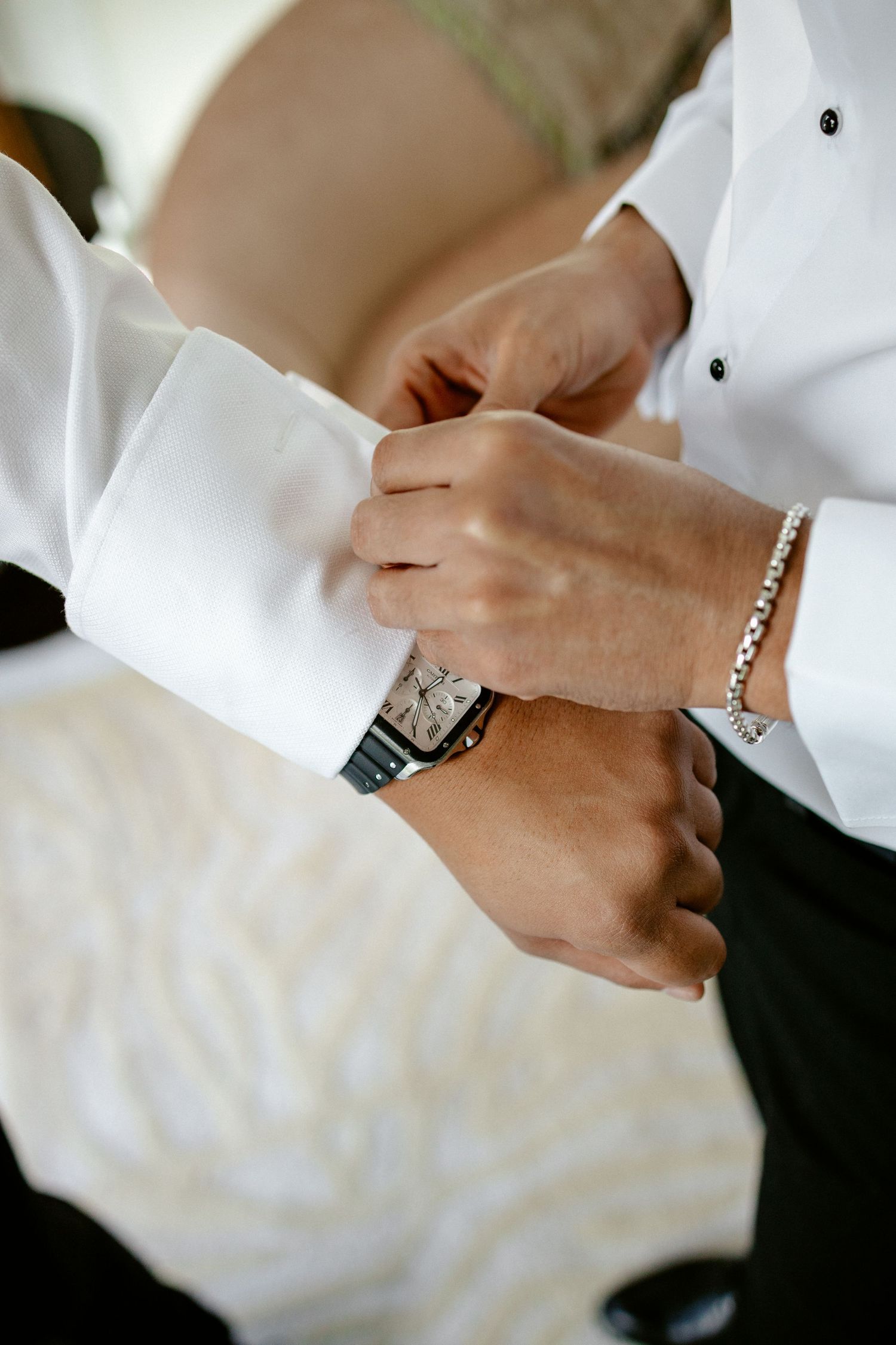 Groom getting cufflinks fastened on white dress shirt while wearing a luxury watch and silver bracelet.