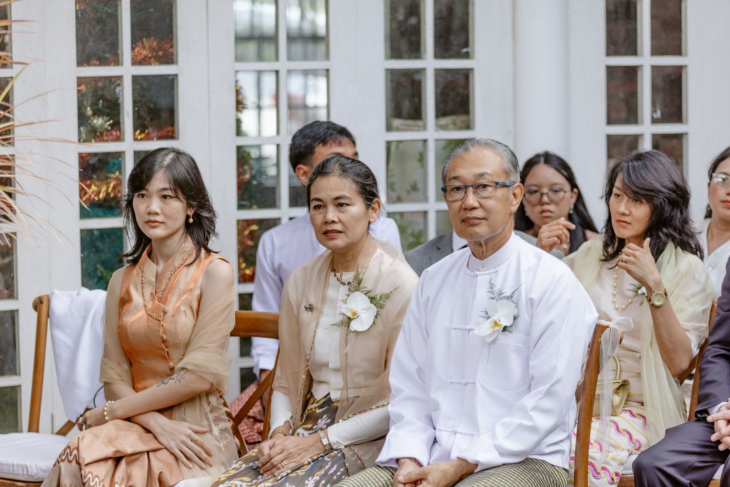 Wedding guests in traditional Southeast Asian attire seated outdoors during a garden wedding ceremony.