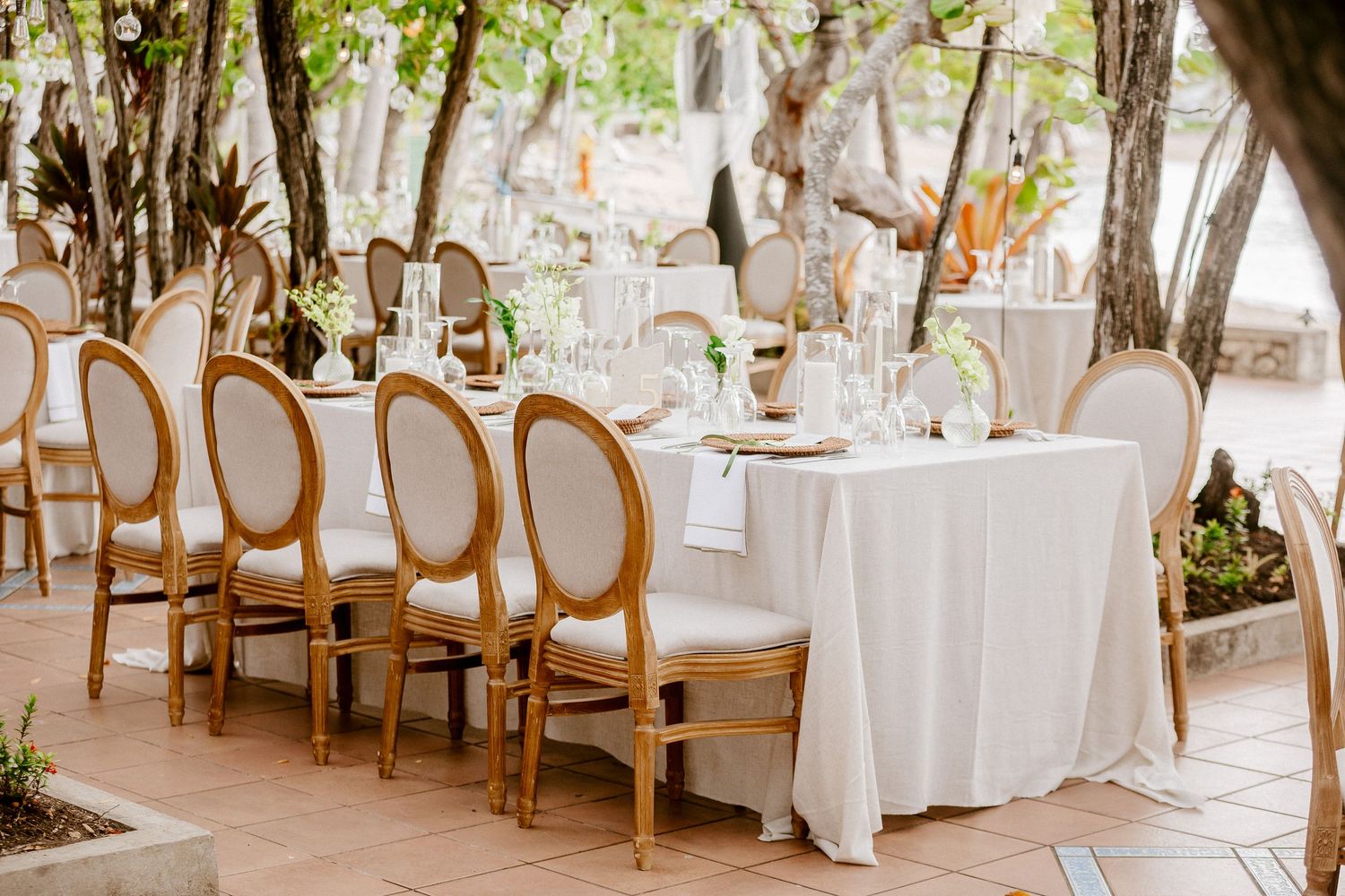 Sophisticated outdoor wedding reception table with gold Louis XVI chairs, white linens, and elegant floral centerpieces.