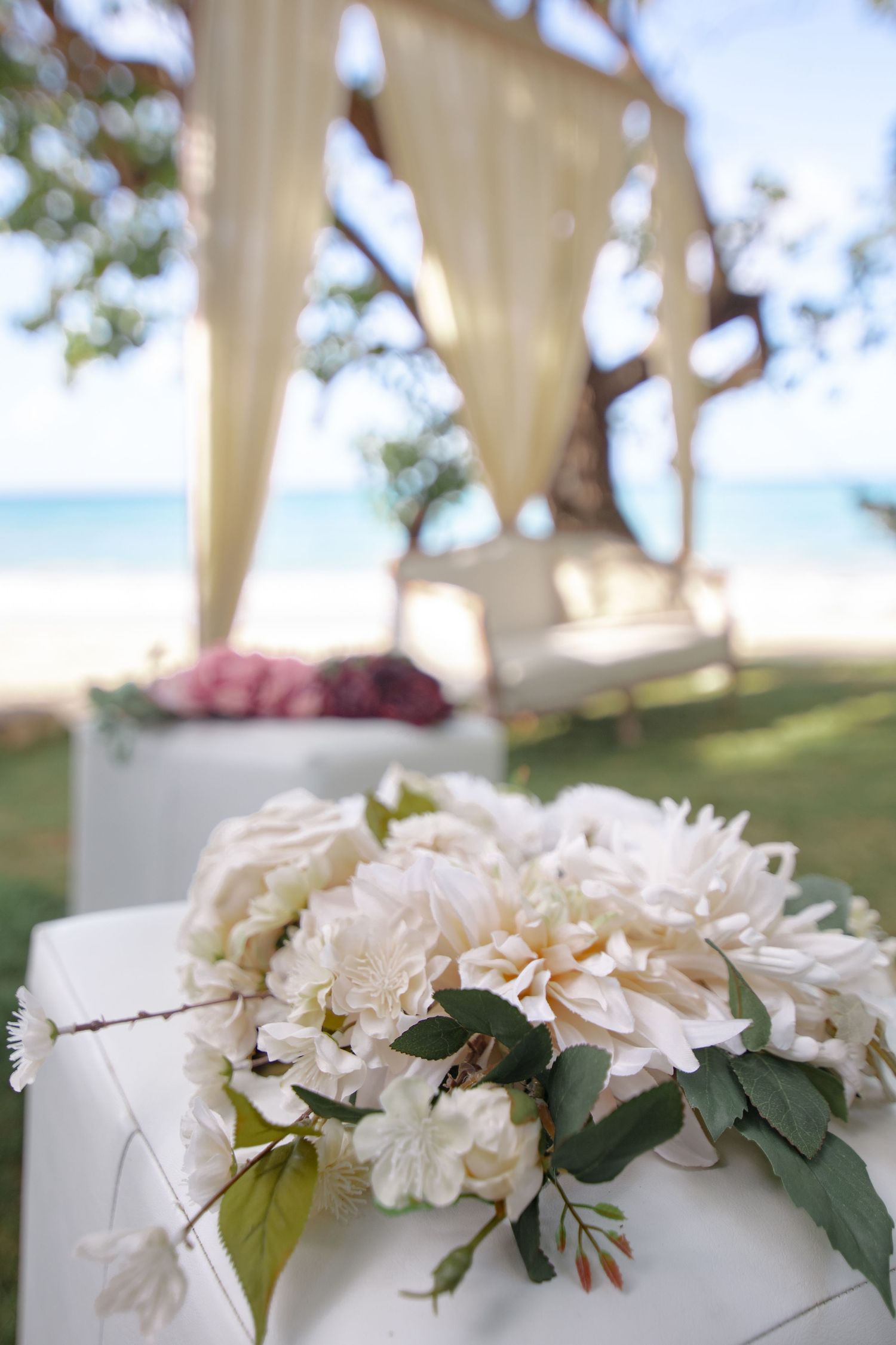White peony bouquet on a pedestal with a beach wedding canopy and ocean backdrop.
