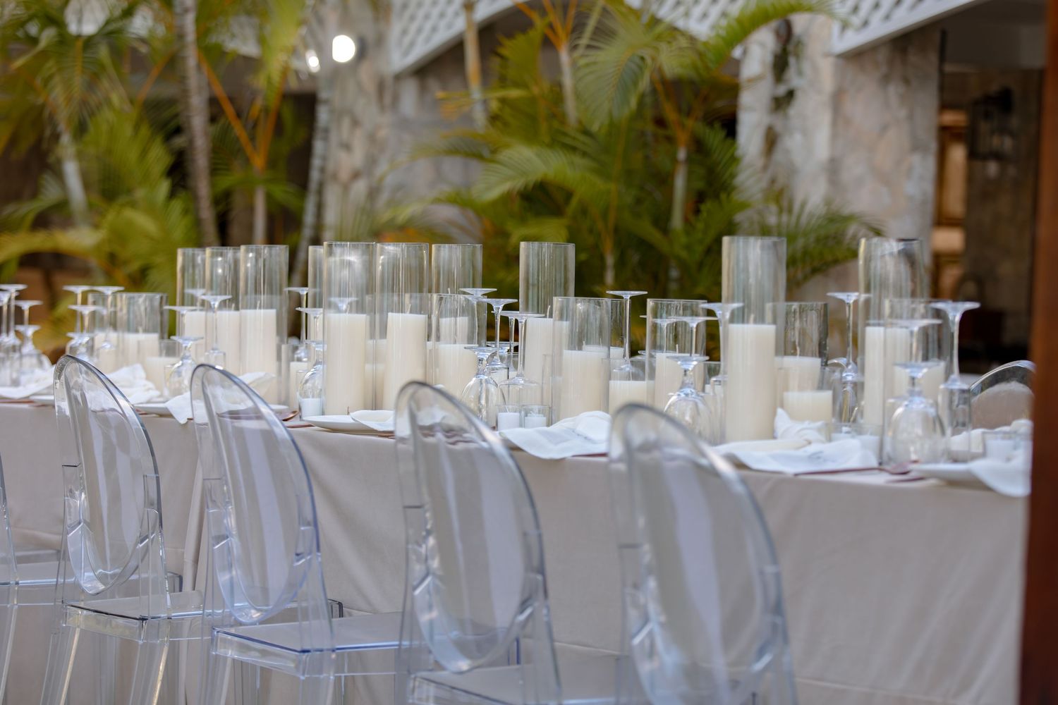 Elegant wedding reception table with white linens, clear ghost chairs, and tall glass cylinder candle centerpieces.