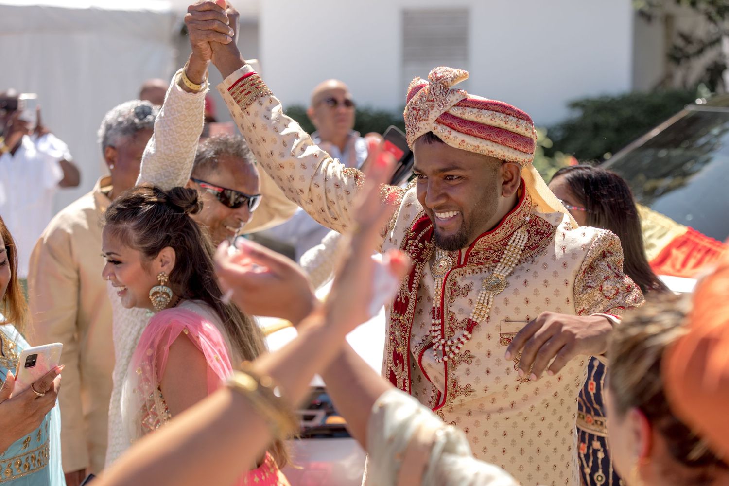 Joyful Indian groom in gold sherwani and turban dancing with guests at outdoor wedding celebration.