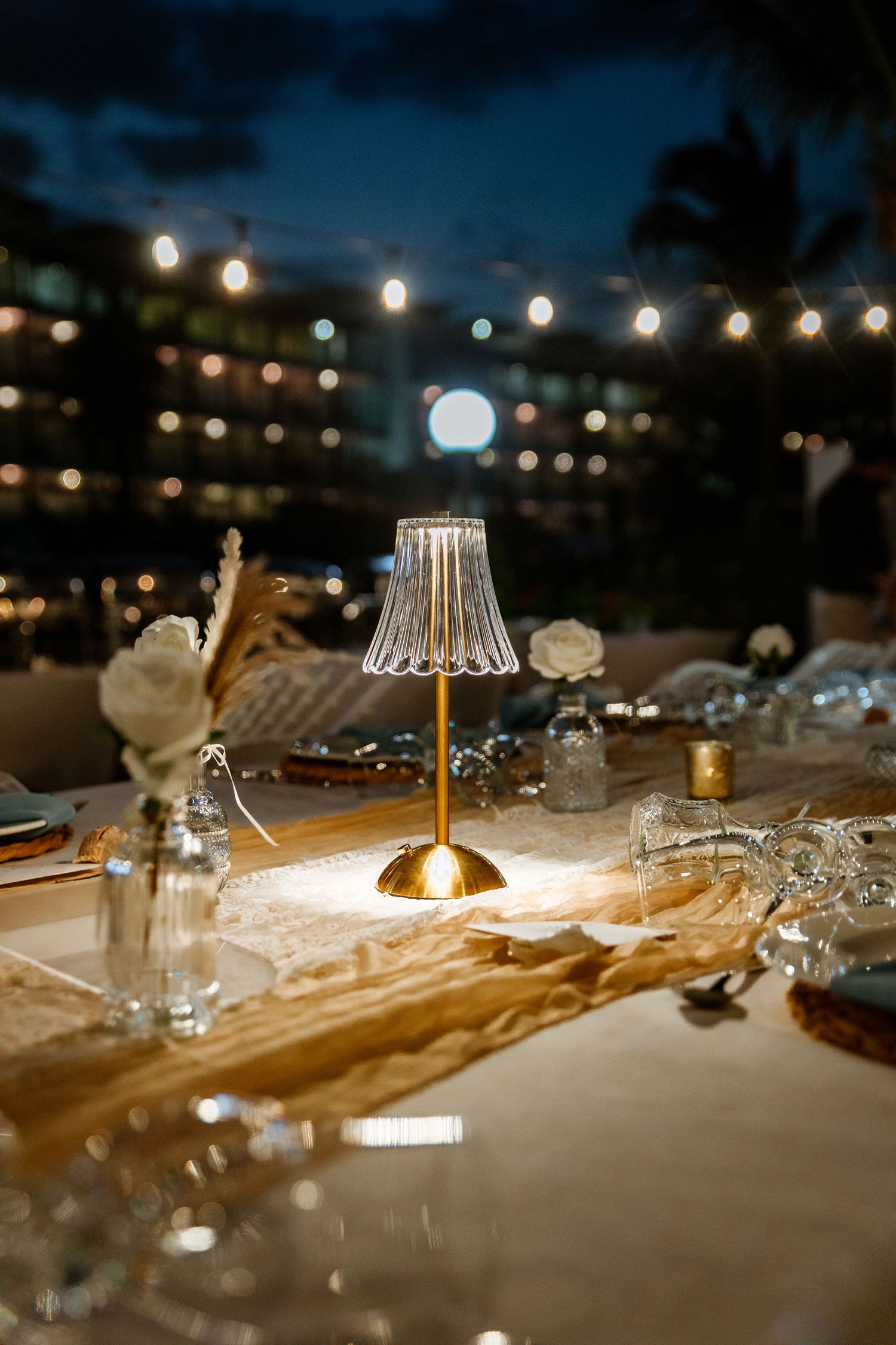 Elegant wedding reception table with gold crystal lamp and string lights at night.