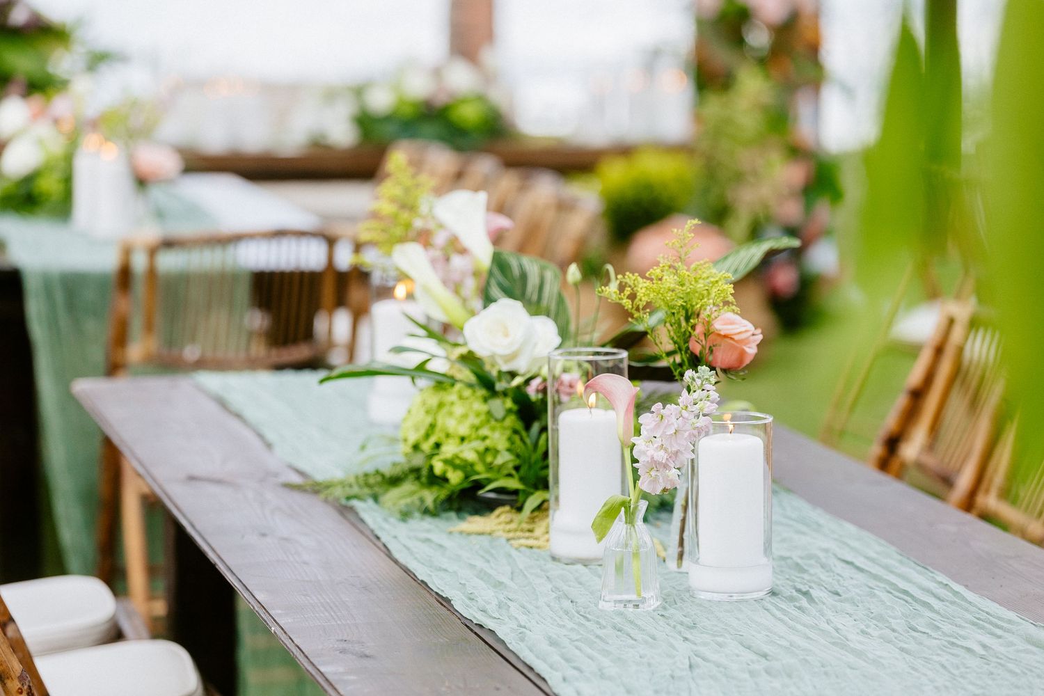 Elegant outdoor wedding table with mint green runner, white candles, and floral centerpiece featuring pink and green blooms.