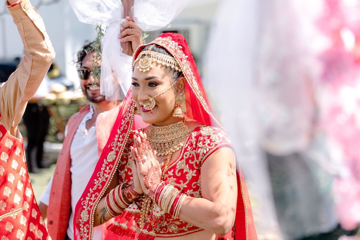 Smiling Indian bride in red and gold lehenga with traditional jewelry during wedding ceremony.