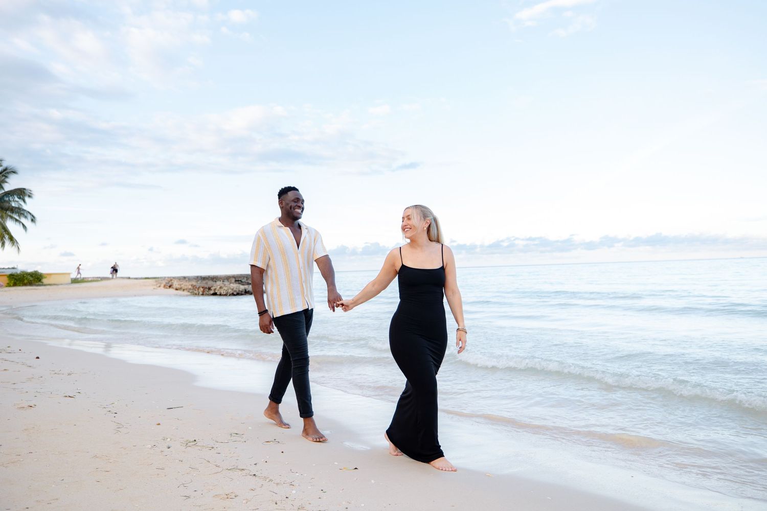 Happy interracial couple walking hand in hand along a tropical beach at sunset.