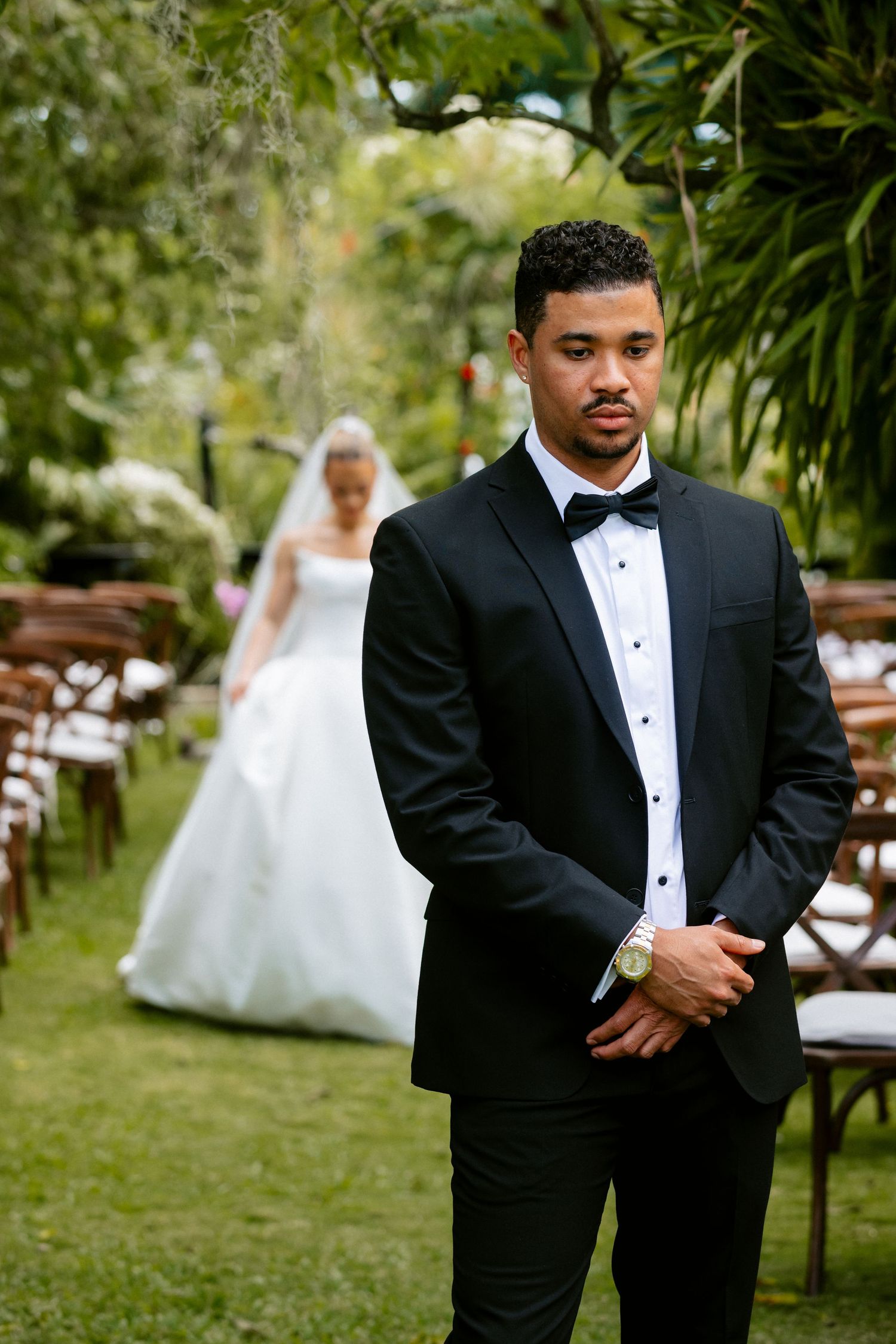 A groom in a black tuxedo stands at the altar as his bride in a white gown approaches down the aisle.