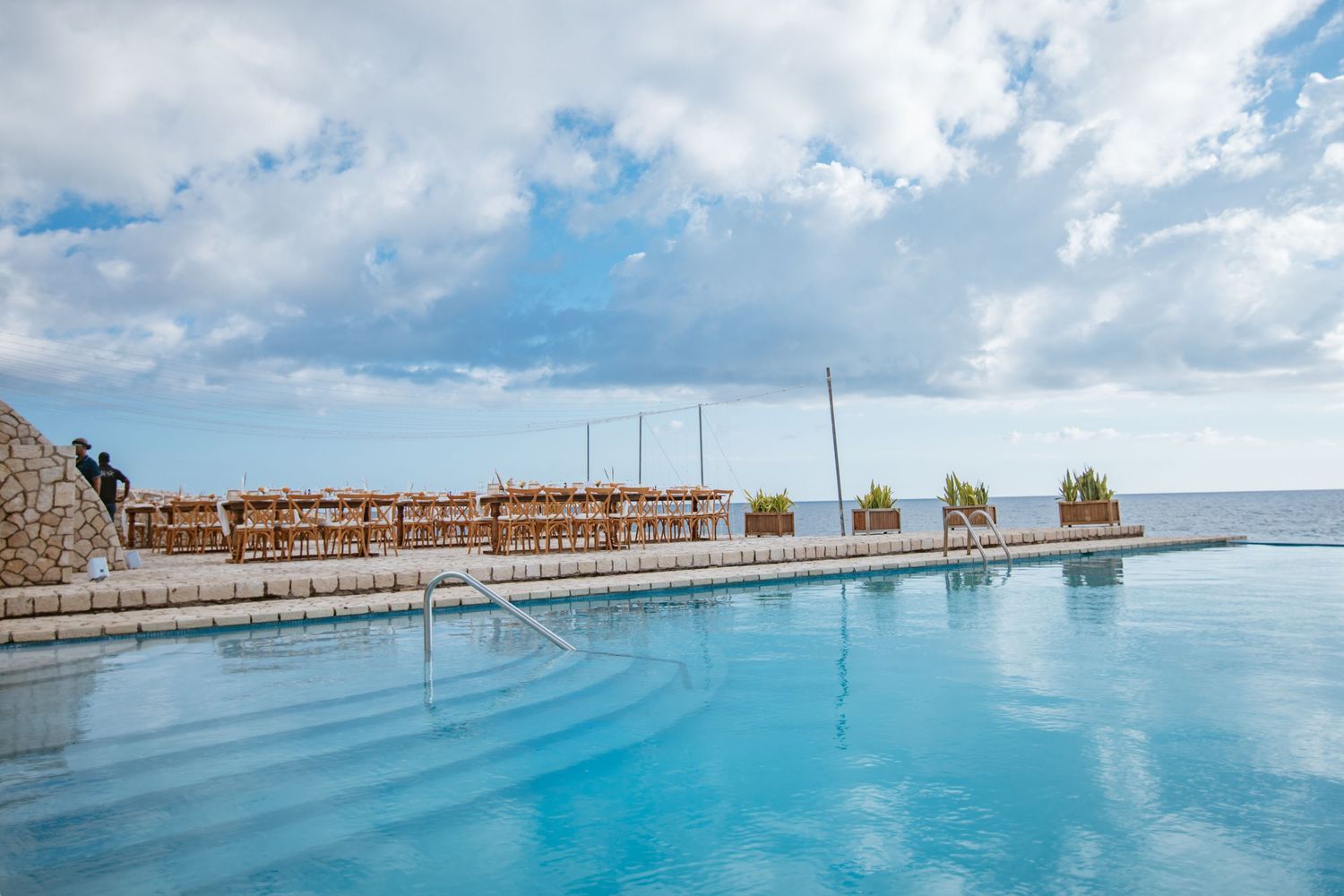 Stunning infinity pool overlooking the ocean with a wooden pergola structure under a dramatic cloudy sky.