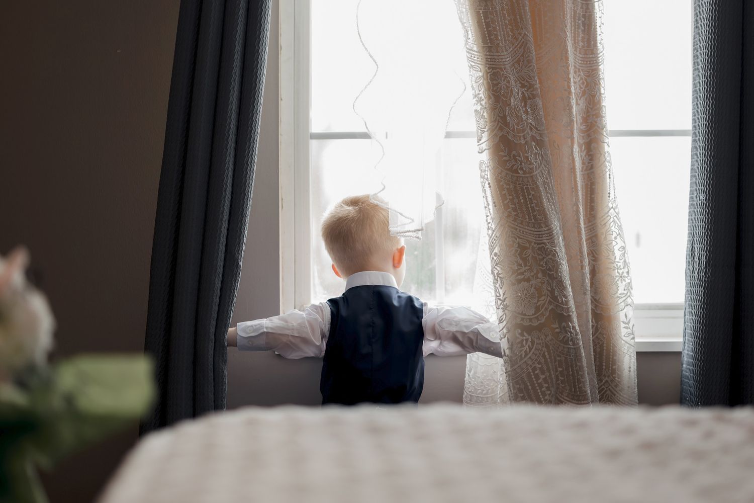 A young ring bearer standing and looking through an arched window.