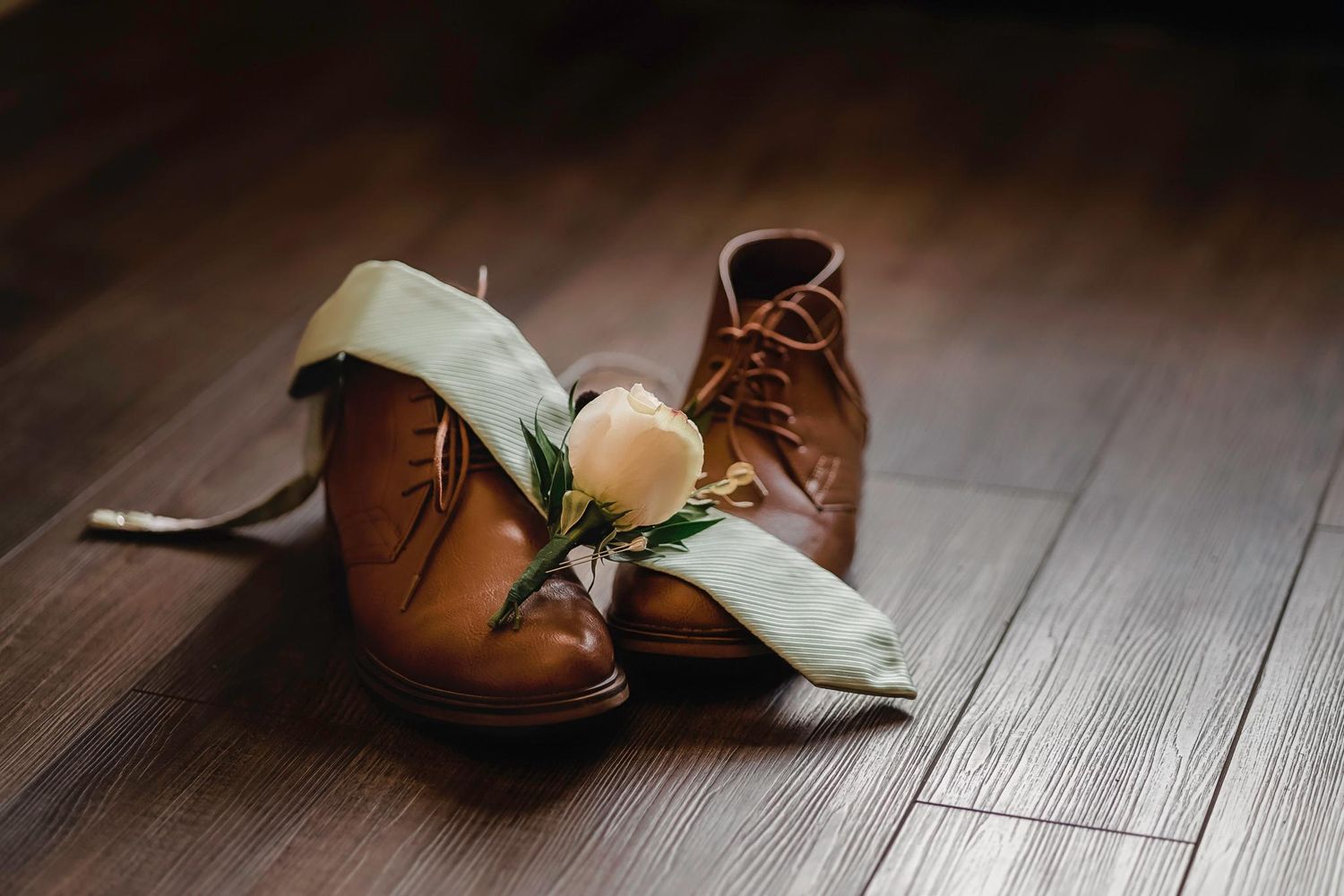 Elegant wedding shoes and a floral boutonniere arranged on a wooden surface.