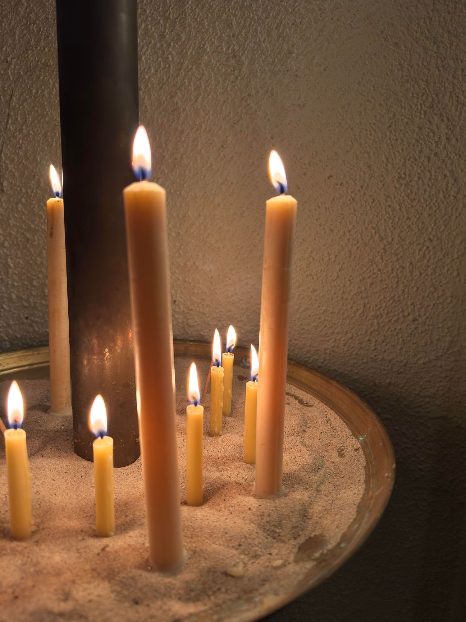 Lit beeswax candles in a brass stand, creating a prayerful atmosphere in an Orthodox church.