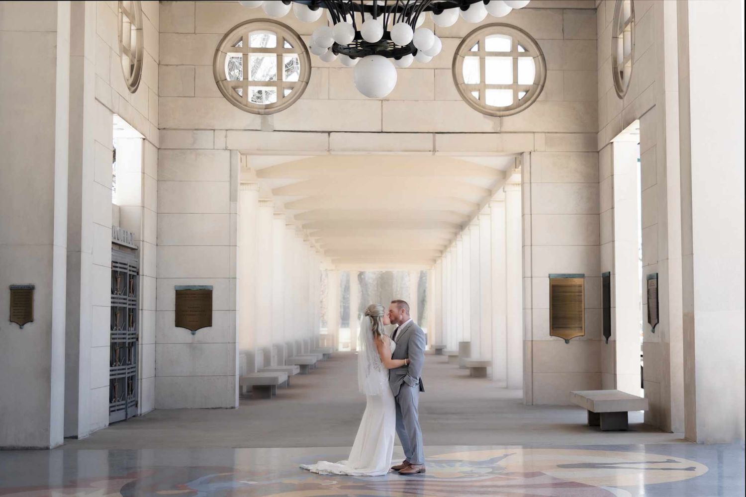 Newlyweds dancing in a grand, high-ceilinged museum hall.