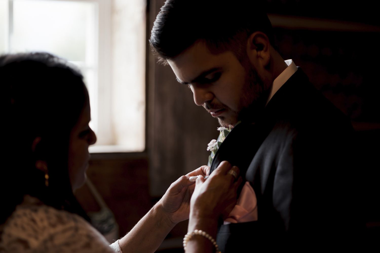 Candid moment of a mother pinning a boutonniere, captured with observant care at an Orthodox wedding.