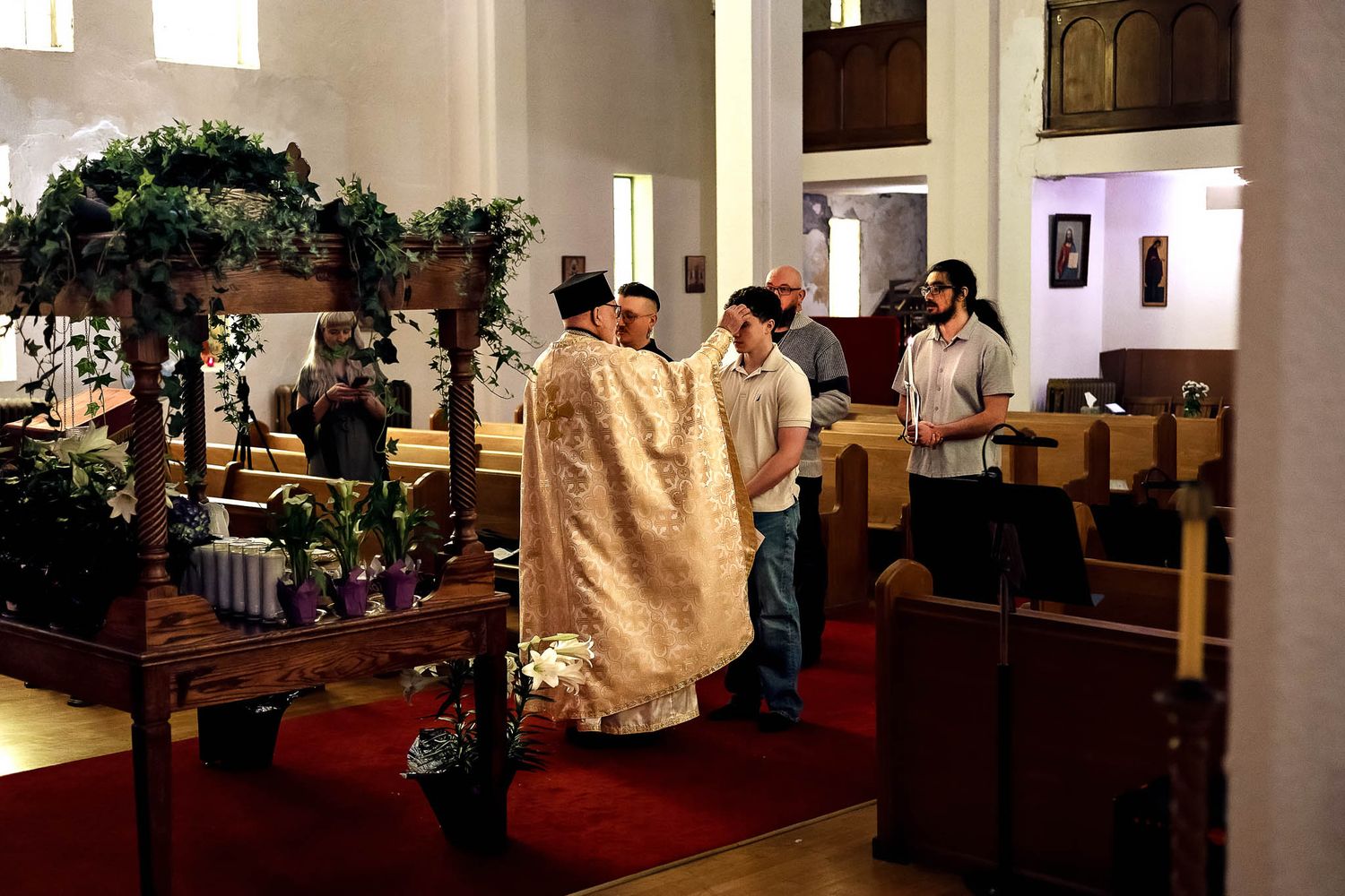 Clergy conducting a sacramental service in a candlelit Orthodox nave.