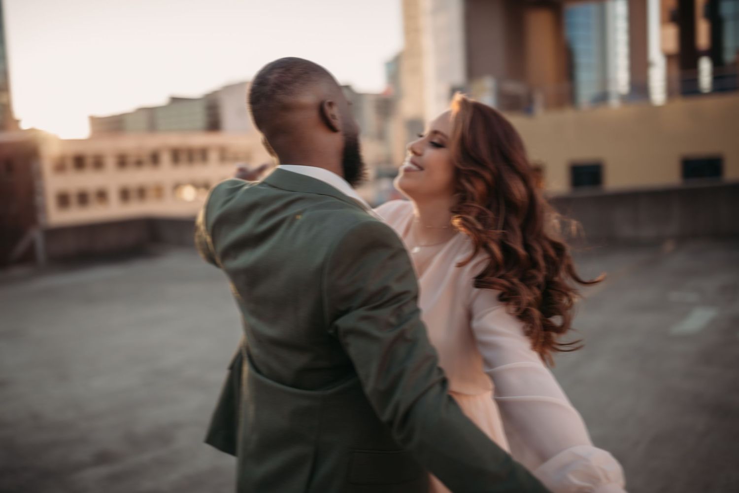 A bride and groom share a romantic dance on a rooftop at sunset with urban buildings in the background.