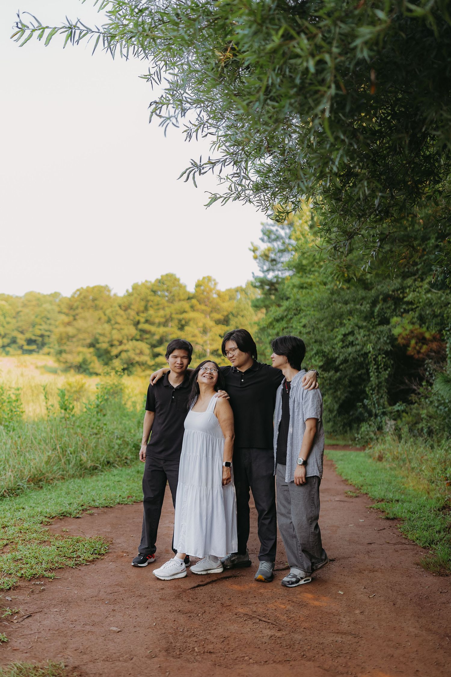 Family of four posing together on a red dirt path surrounded by lush green trees and fields.