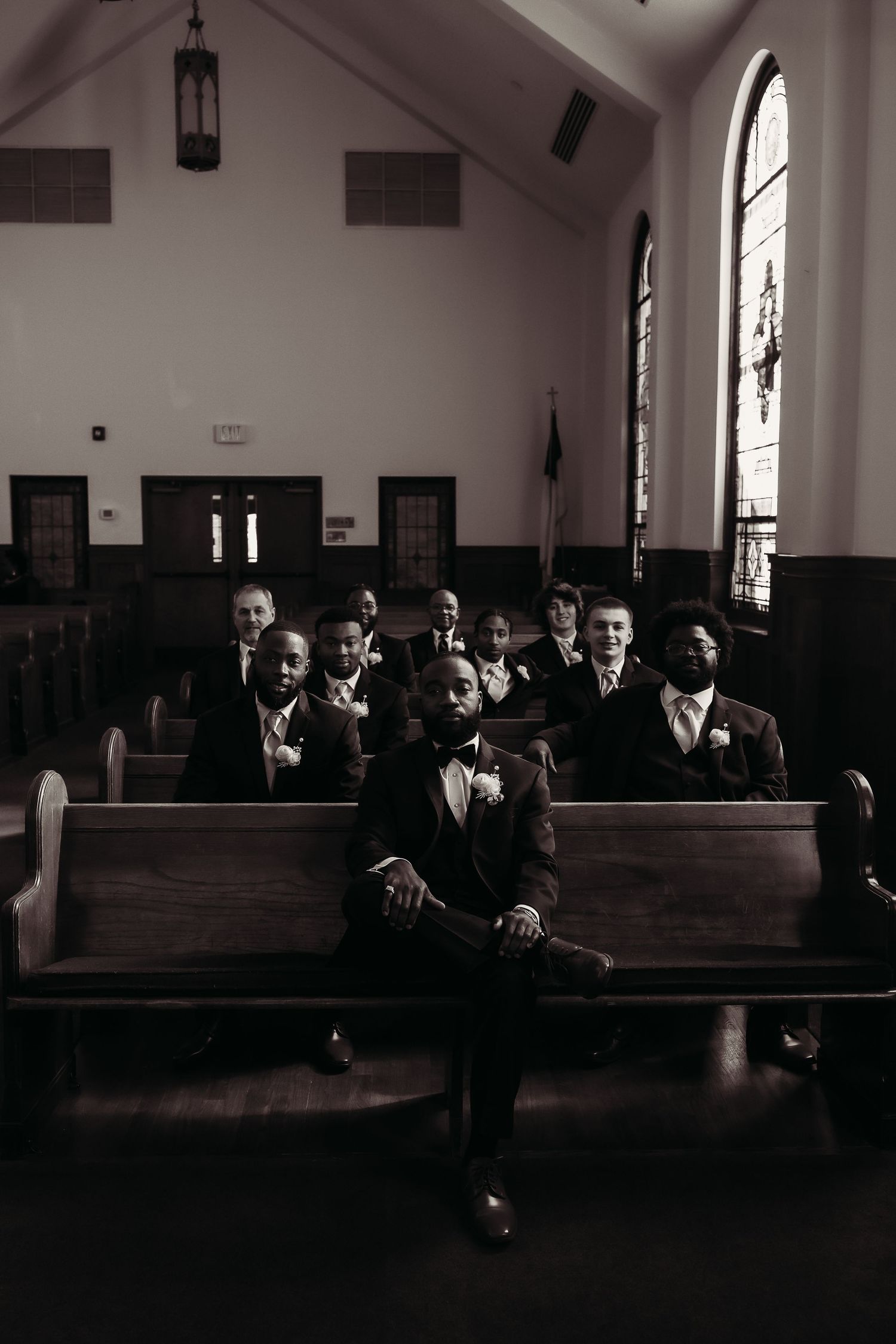 Groom and groomsmen pose in a classic black and white portrait inside a traditional church with stained glass.
