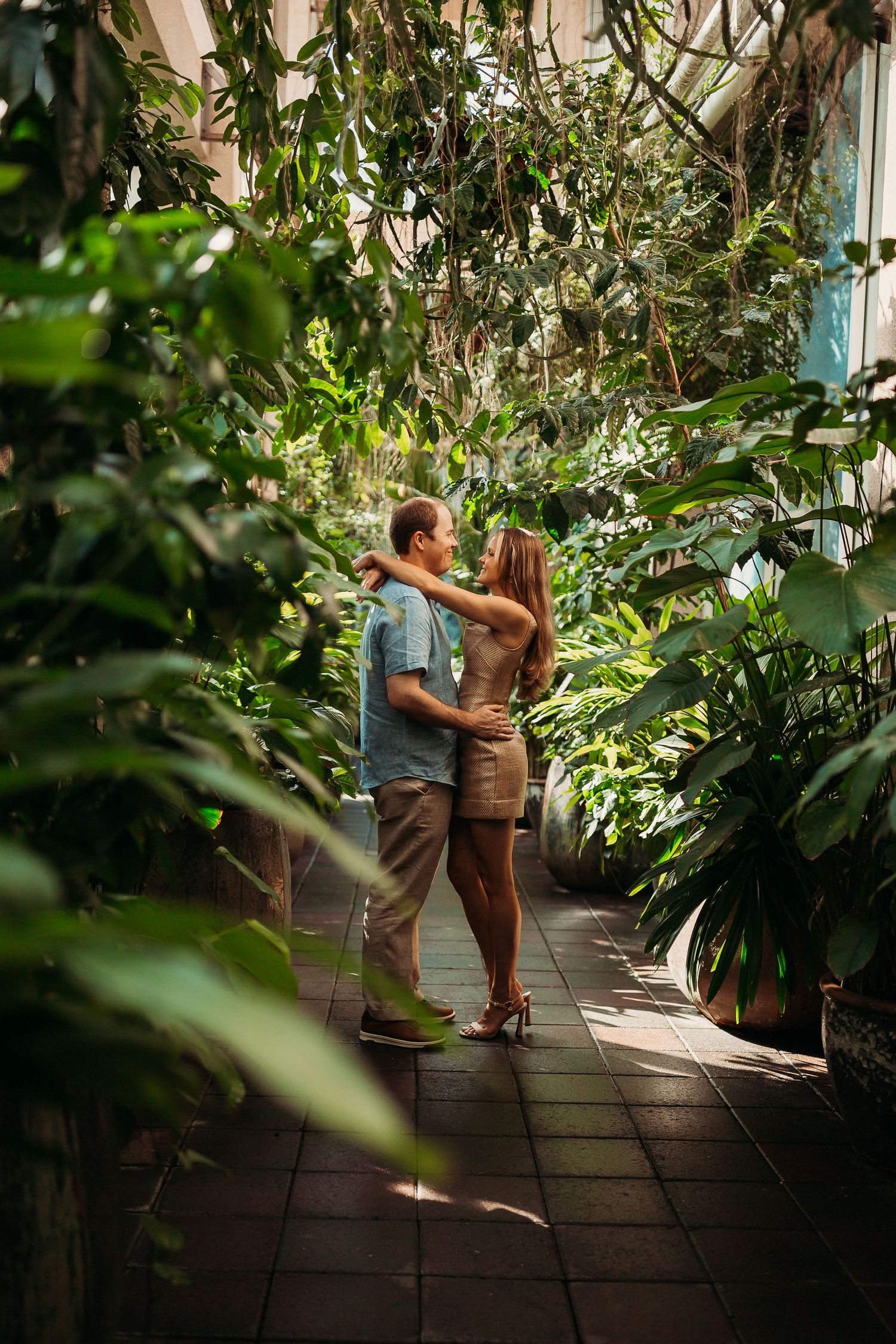Romantic couple embracing and dancing in a lush tropical greenhouse garden setting.