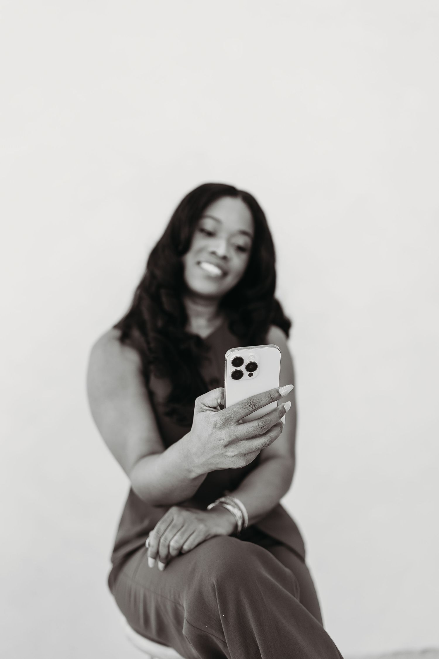 Smiling woman with long hair looking at her smartphone against a light background.