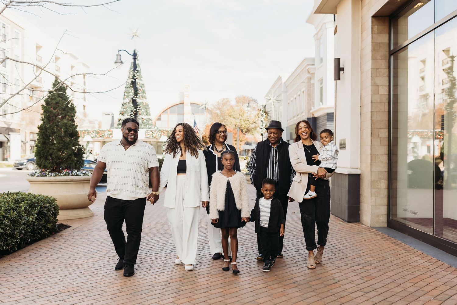 Black family in white and black outfits walking together on a brick sidewalk in an outdoor shopping area.