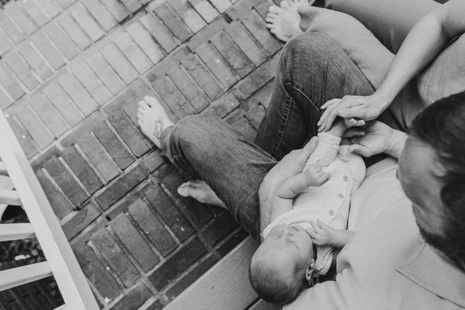 Black and white photo of adult lying on brick porch floor with newborn baby being tended to by caregiver.