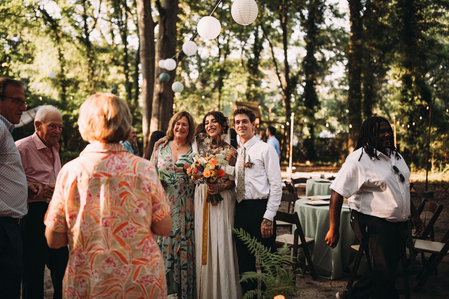 Wedding couple greeting guests at an outdoor woodland ceremony with string lights above.