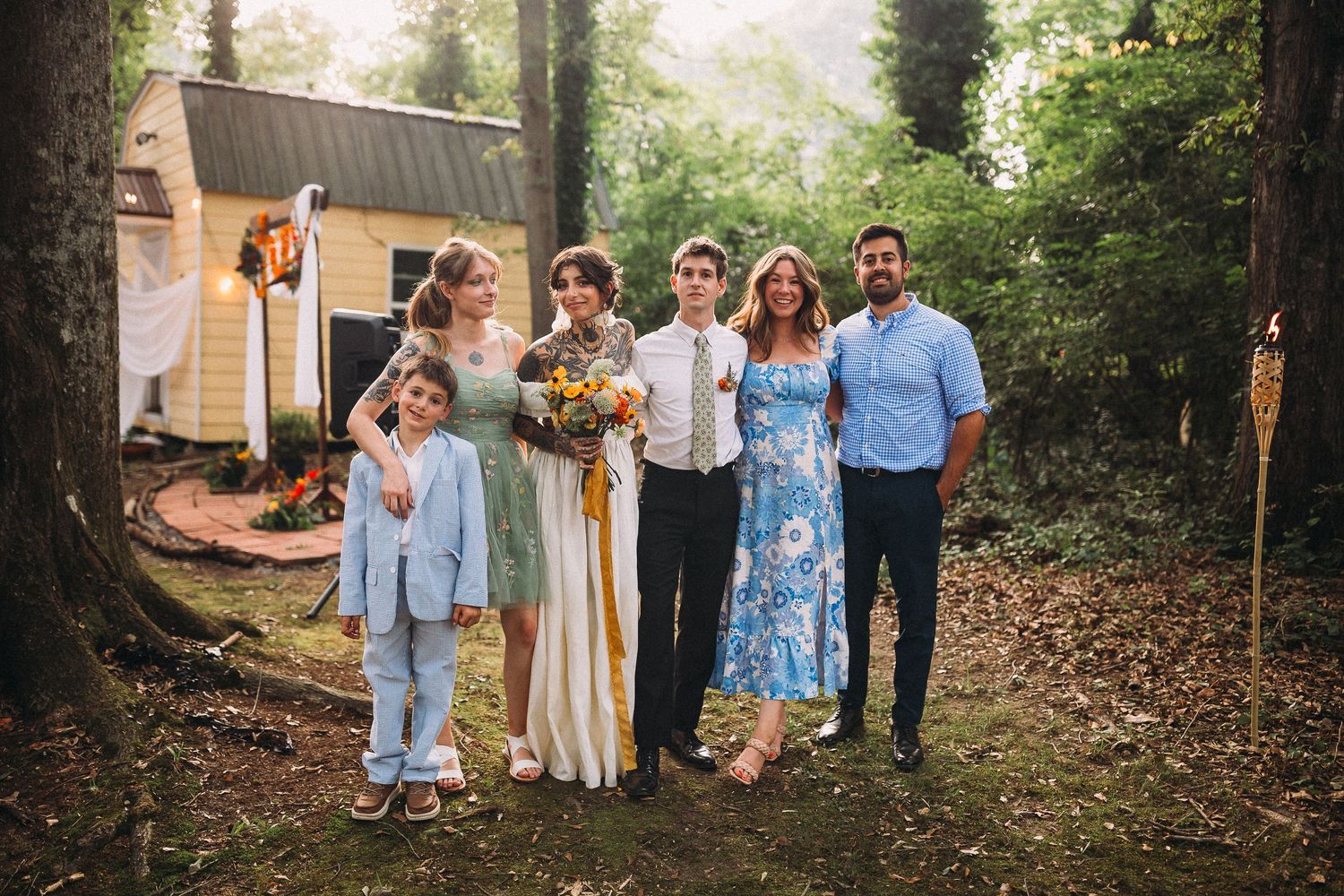 Wedding couple posing with family members in front of a yellow cabin in a wooded setting.